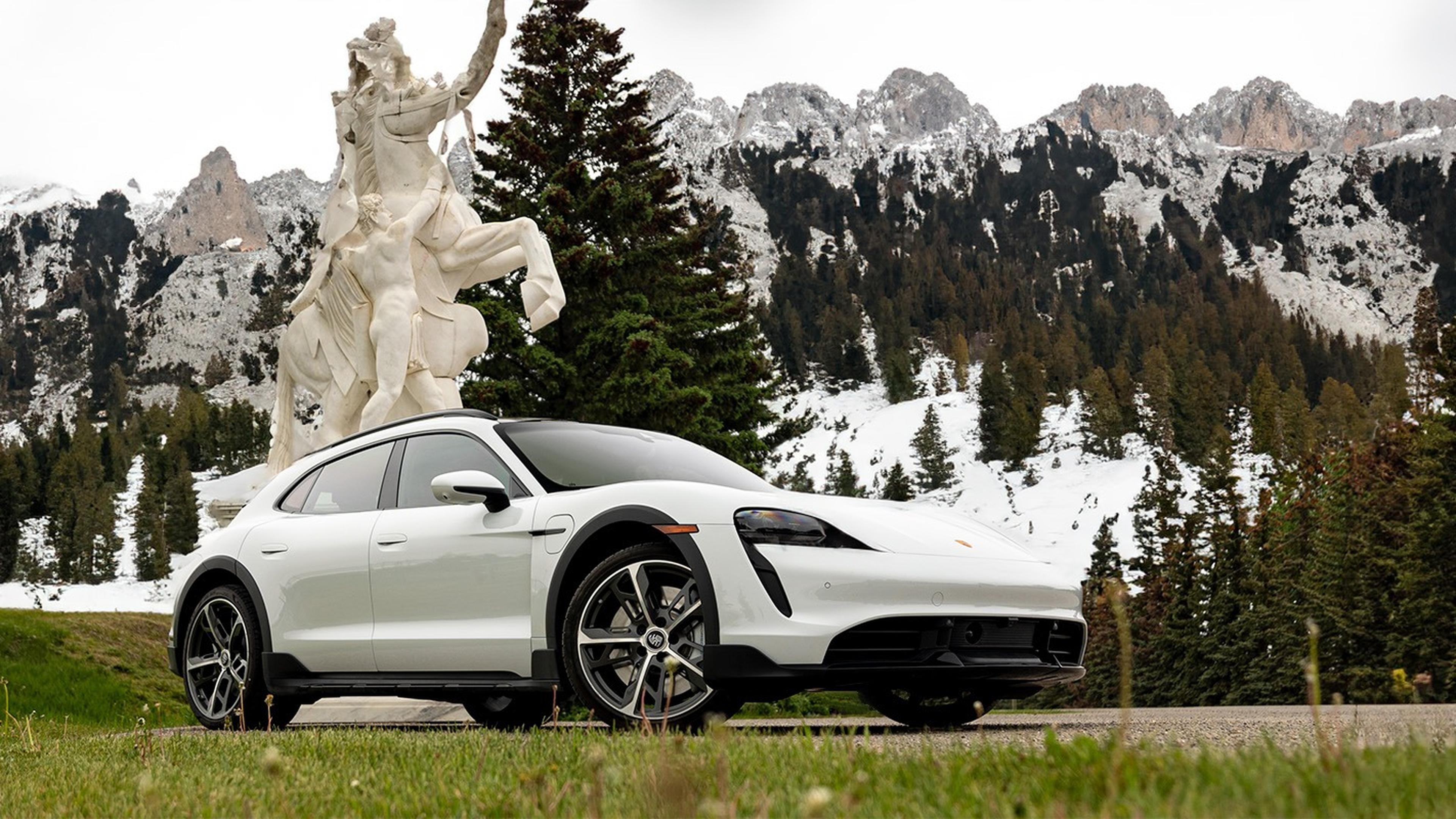 A sleek Taycan Cross Turismo parked in front of a large statue, with snow-capped mountains and evergreen trees in the background.