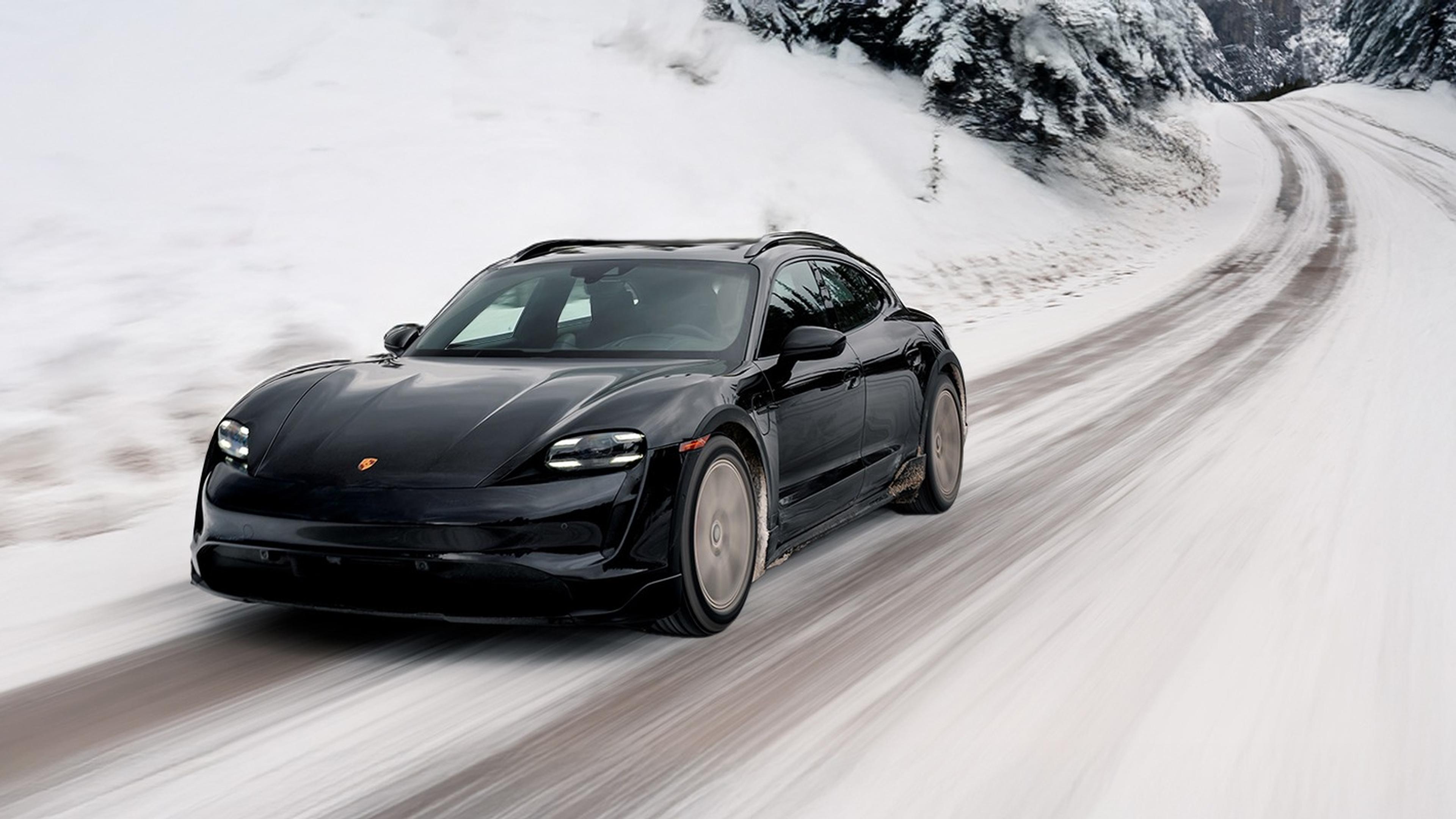 A black Taycan driving on a snowy forest road, surrounded by snow-covered trees and banks.