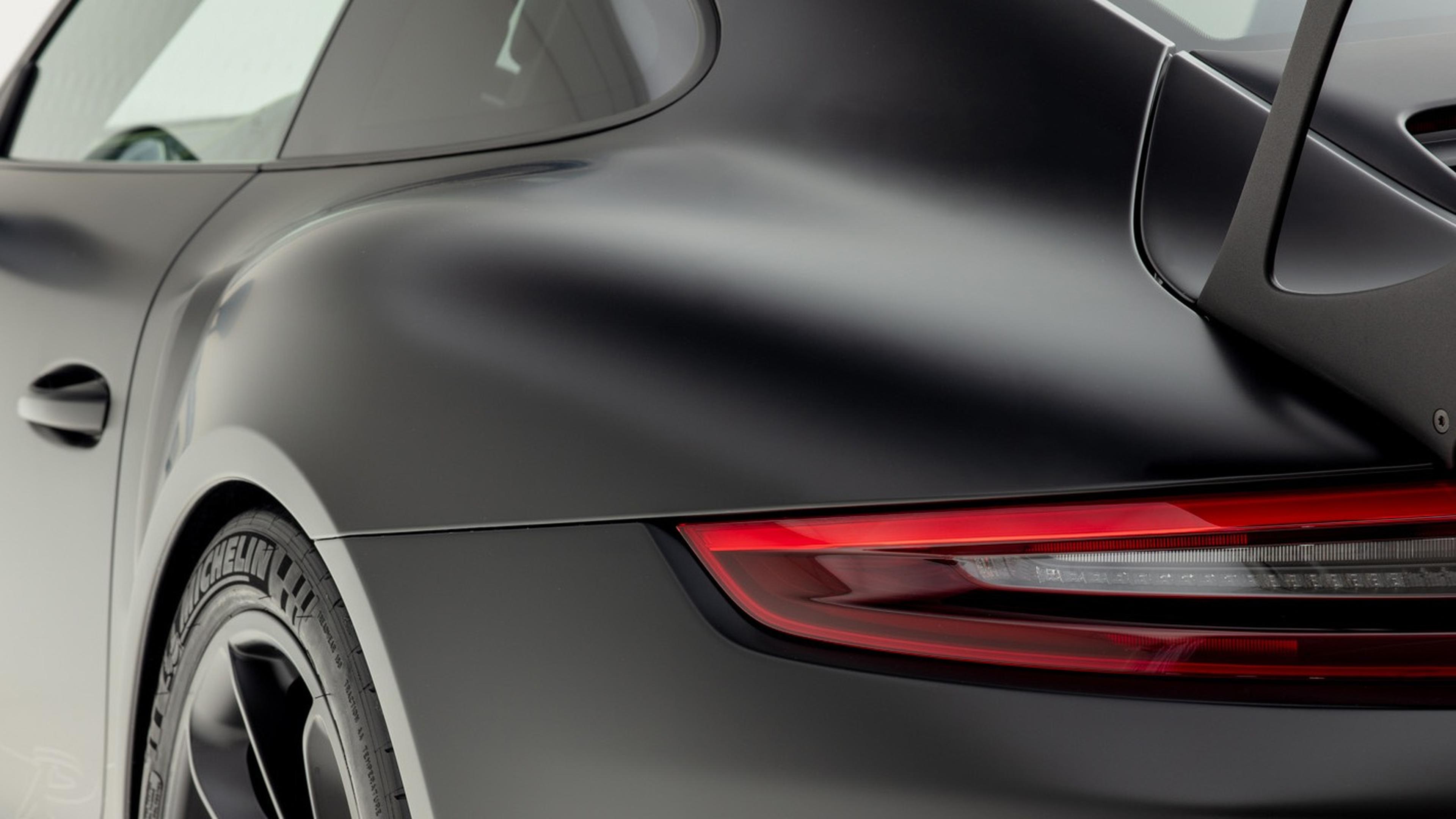 Matte Wrapped PPF on a GT3 RS Close-up of the rear side of a sleek black sports car with a red taillight, showing aerodynamic curves and branding on the tire.