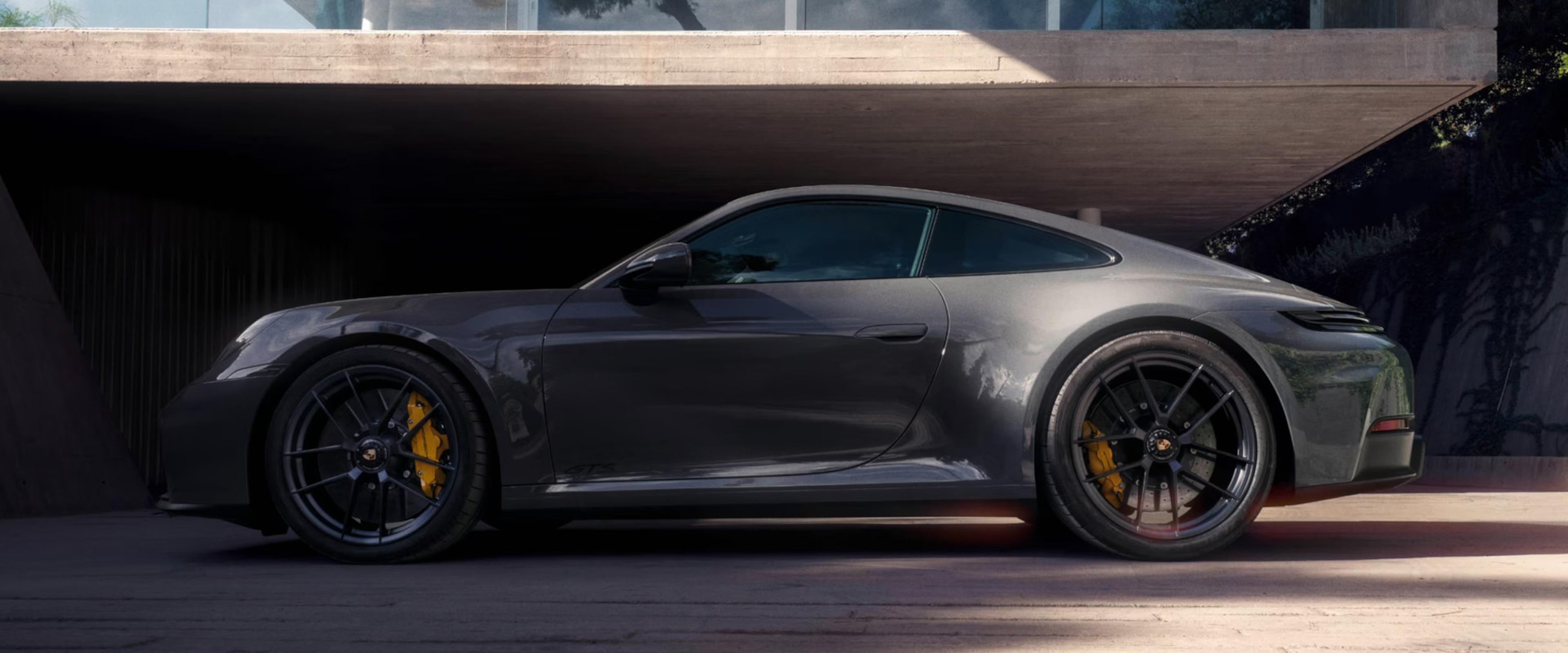 Sleek gray sports car with yellow brake calipers parked in front of a modern concrete structure, viewed from the side.