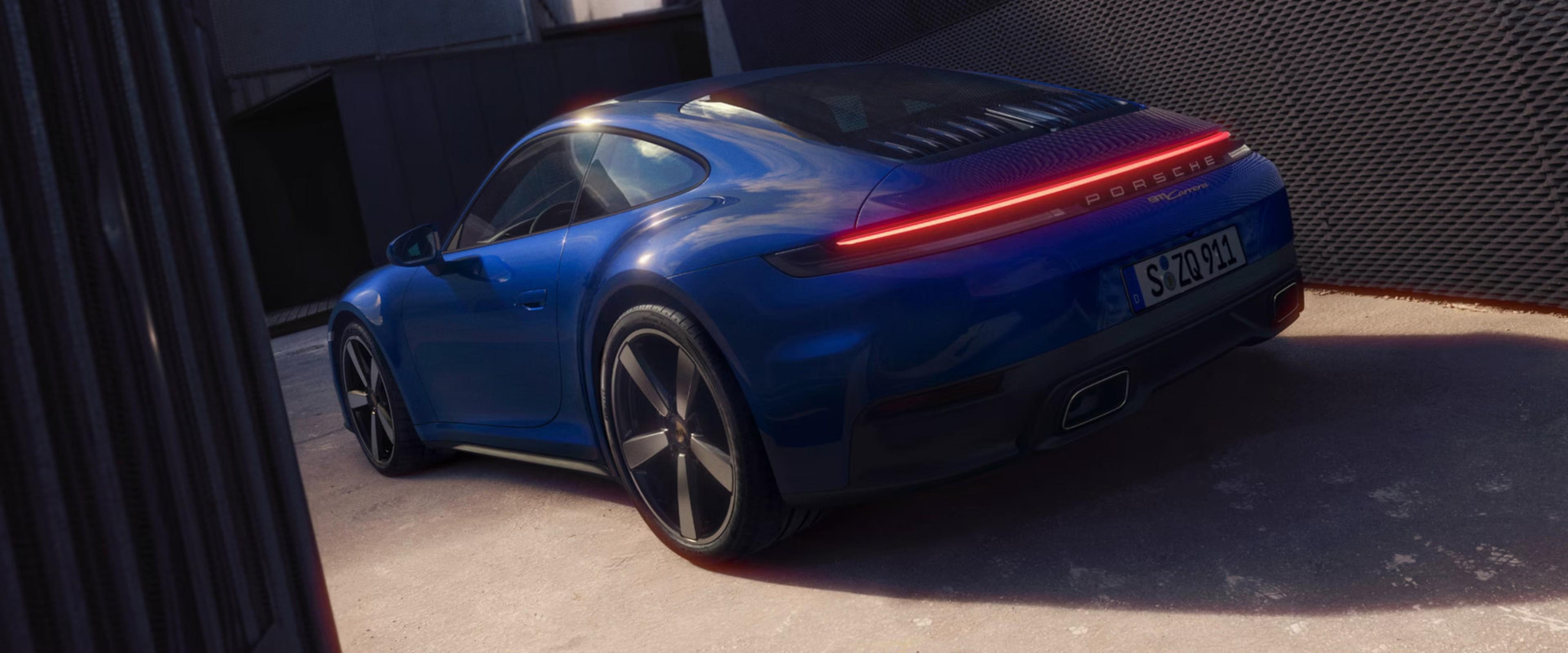 A sleek blue sports car with tinted windows, polished rims, and a distinctive rear light design, parked in a modern setting.