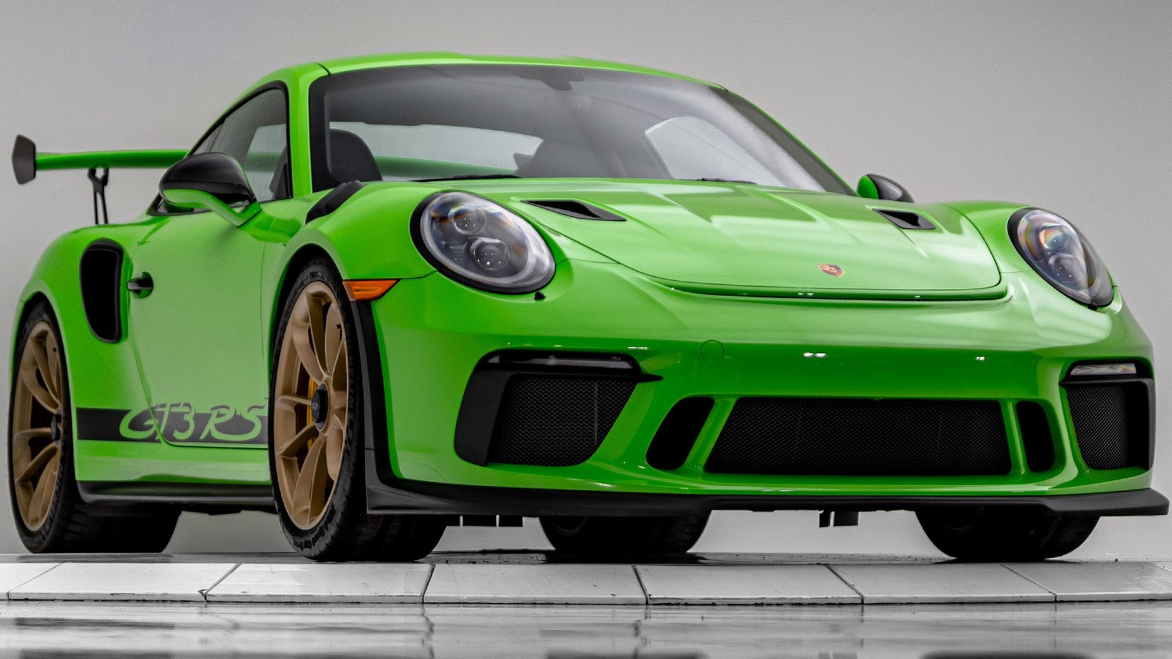 Porsche 911 GT3 RS with black details and a large rear spoiler, displayed on a white platform.