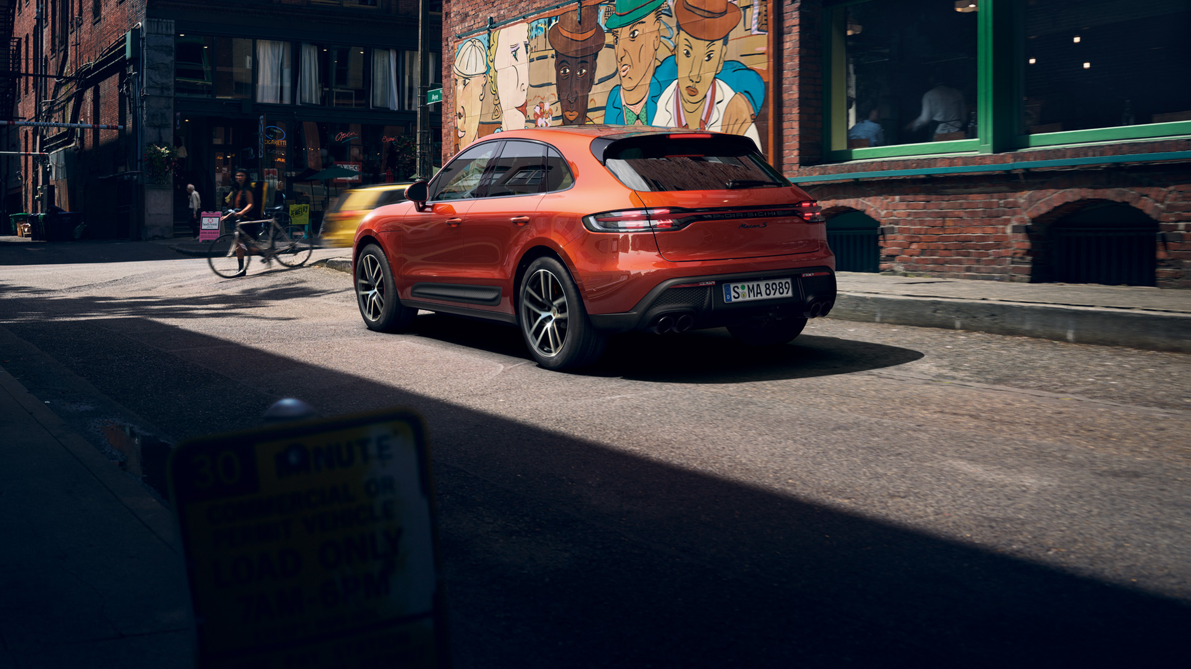 Porsche Macan S in Papaya Metallic parked on a city street.