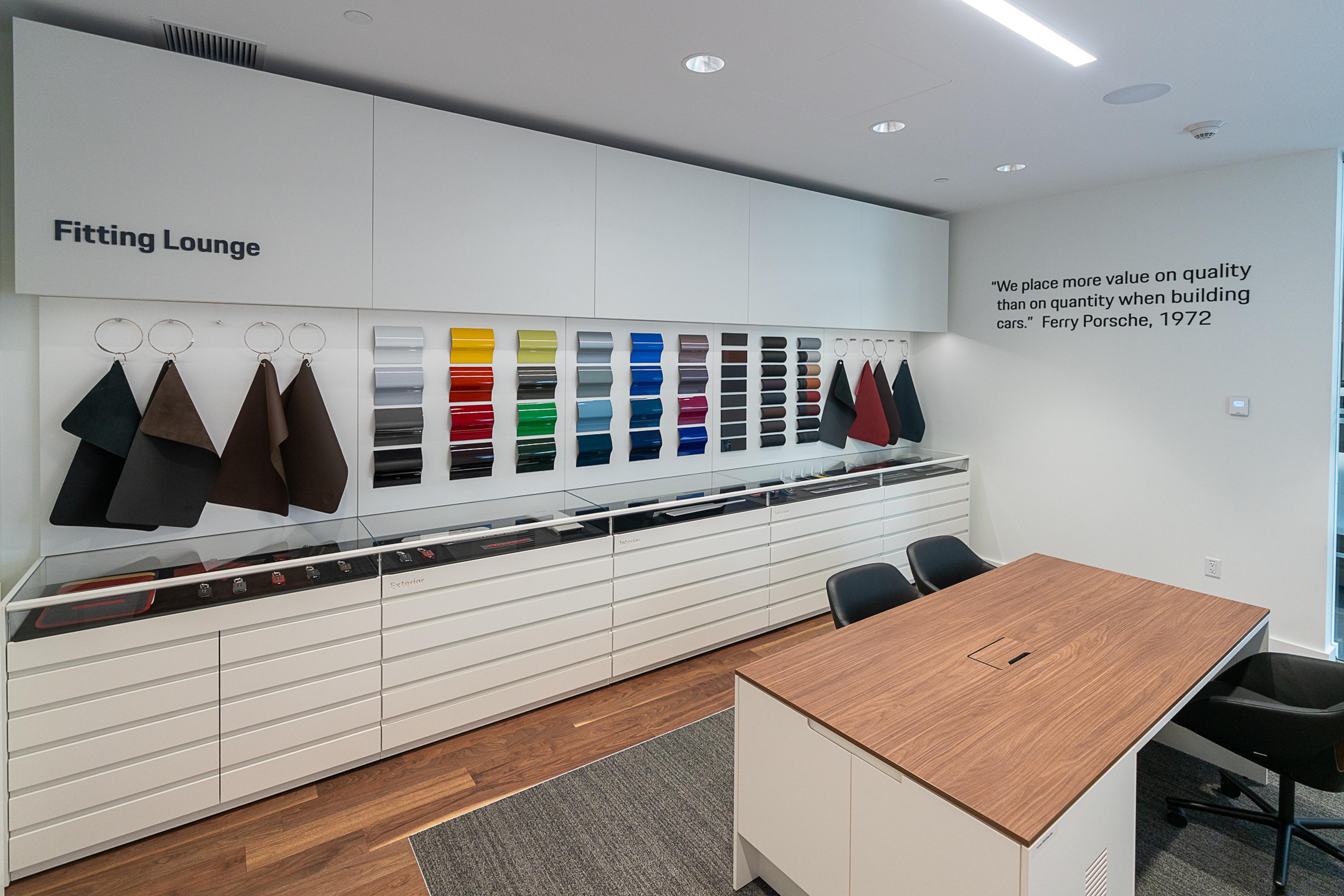 Modern fitting lounge with fabric and color samples, sleek storage drawers, and a wooden table. Quote on wall emphasizes quality in car building.