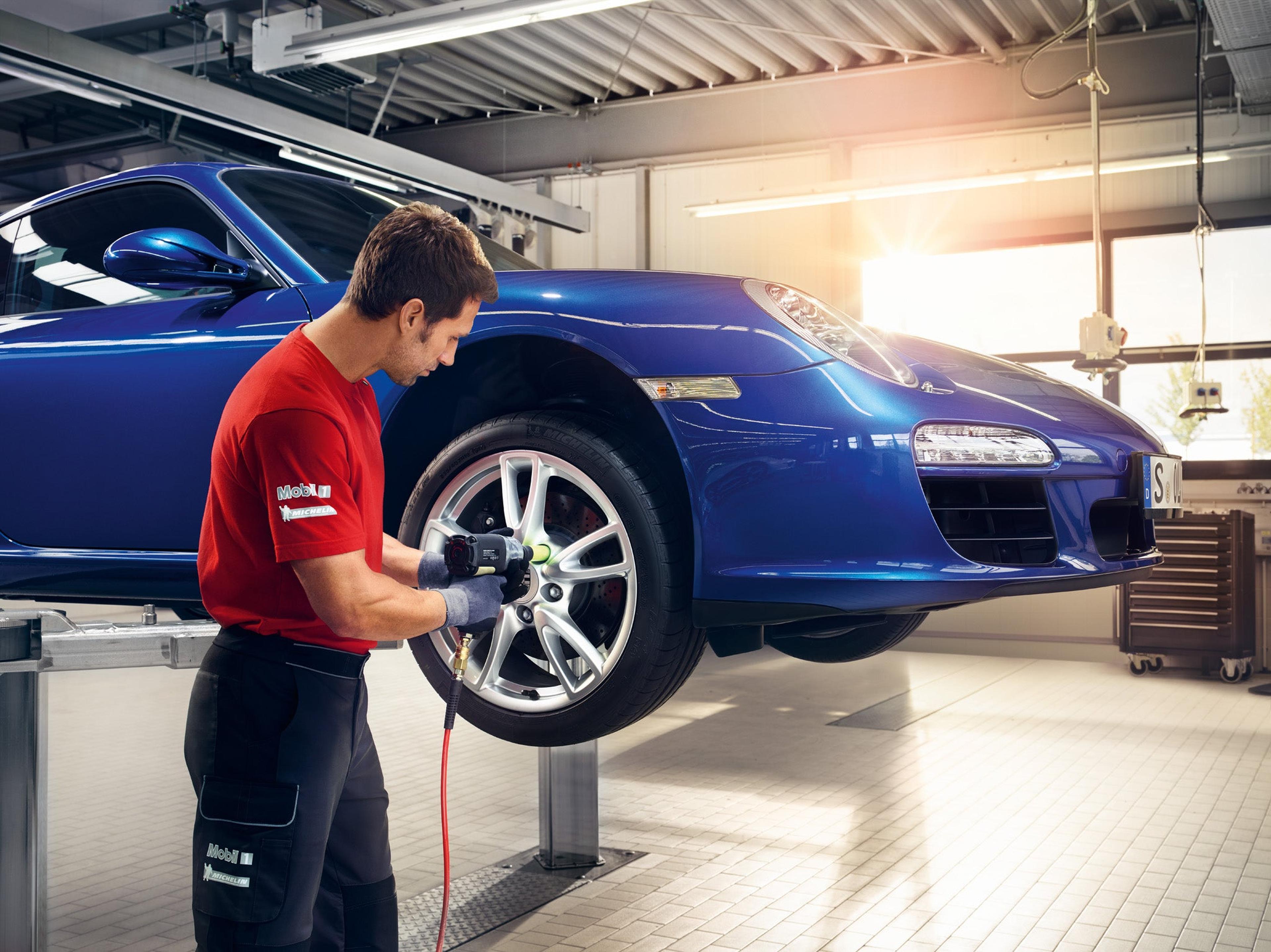 Technician performing a four-wheel alignment on a blue Porsche
