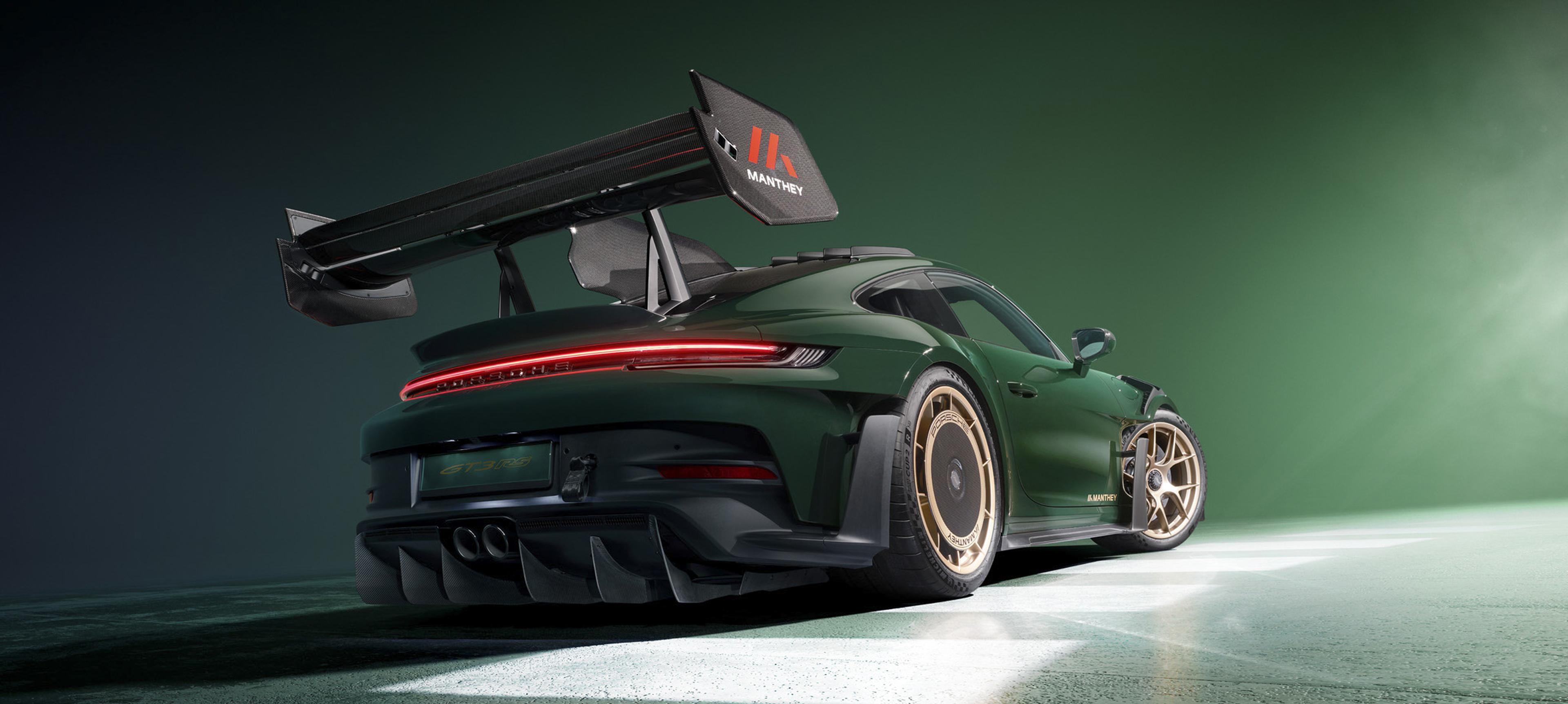 Rear three-quarter view of a green Porsche 911 GT3 RS equipped with Manthey performance components, including a large rear wing and aerodynamic upgrades.