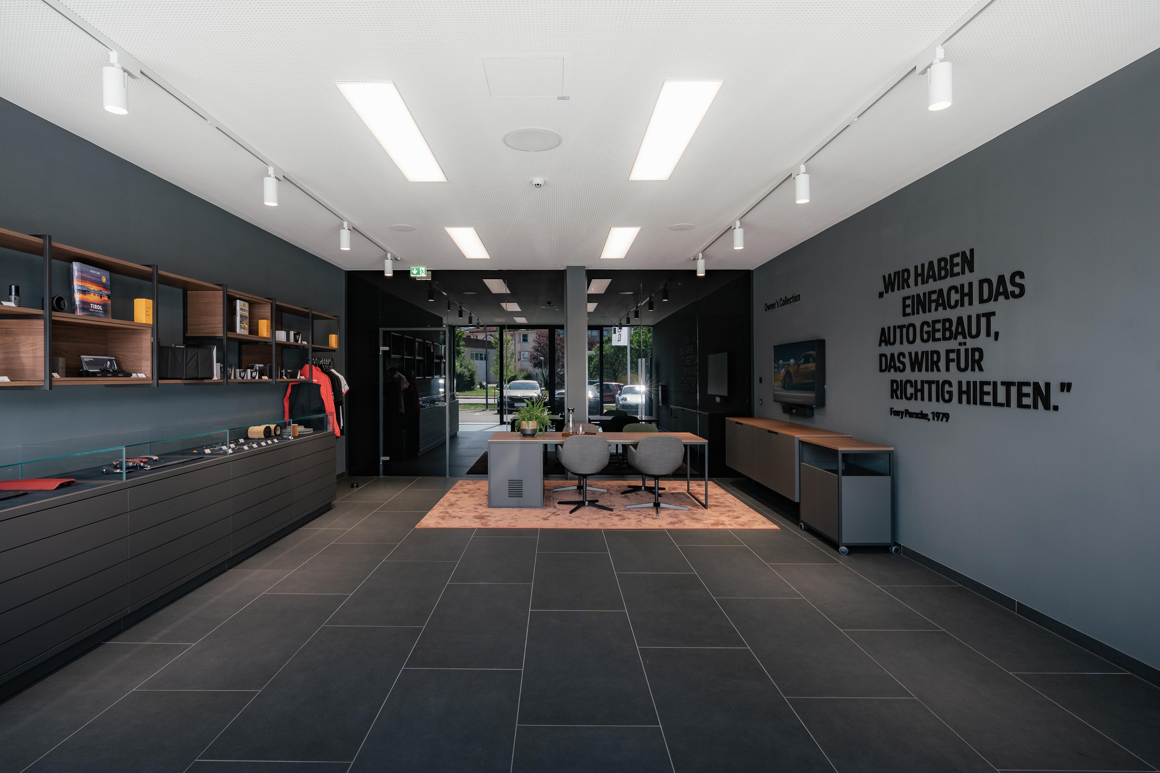 Modern showroom interior with sleek black tiles, wall displays of automotive memorabilia, a seating area, and a large window view.