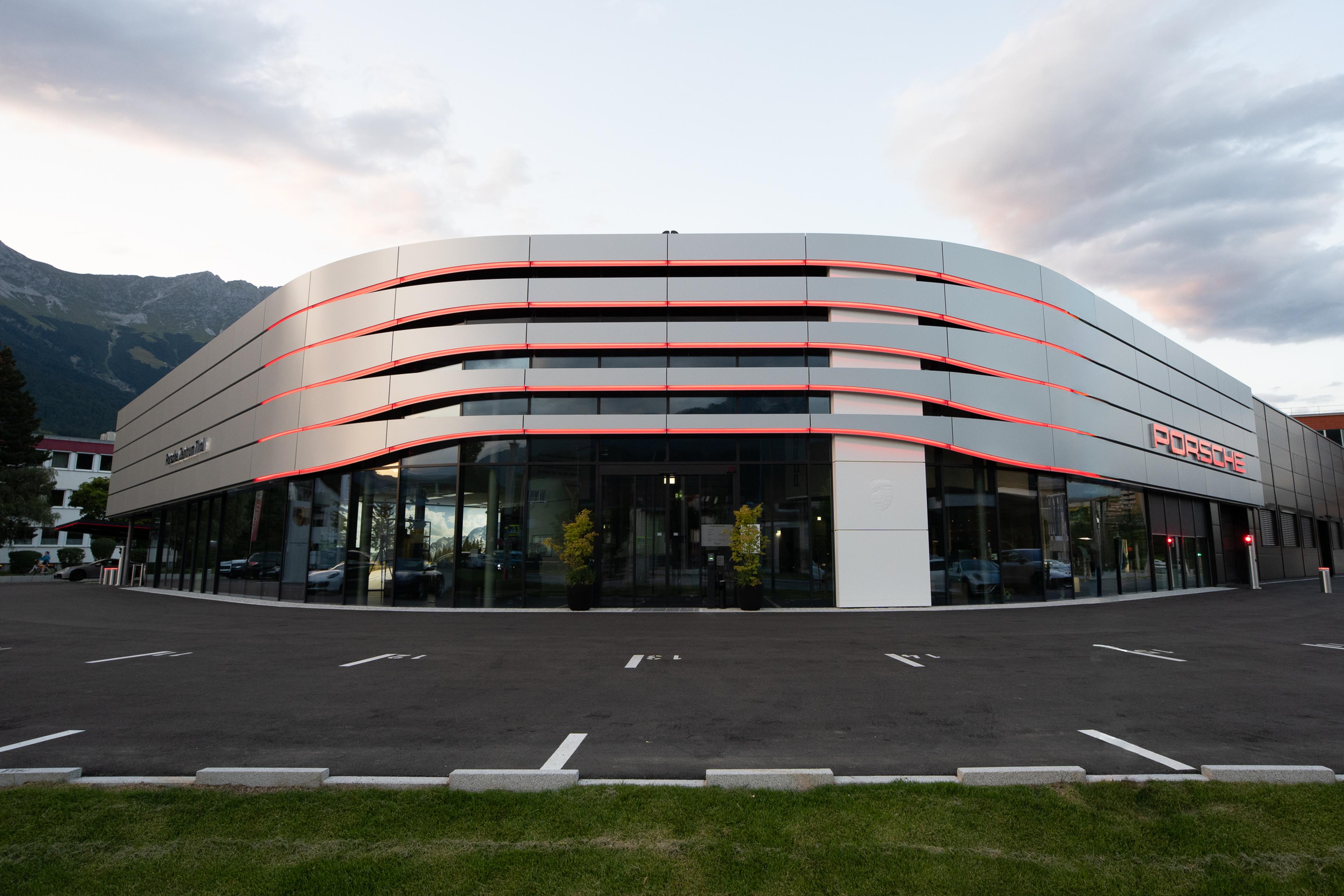 Modern building with sleek, curved design, featuring large glass windows, red accents, empty parking lot, and mountains in the background.