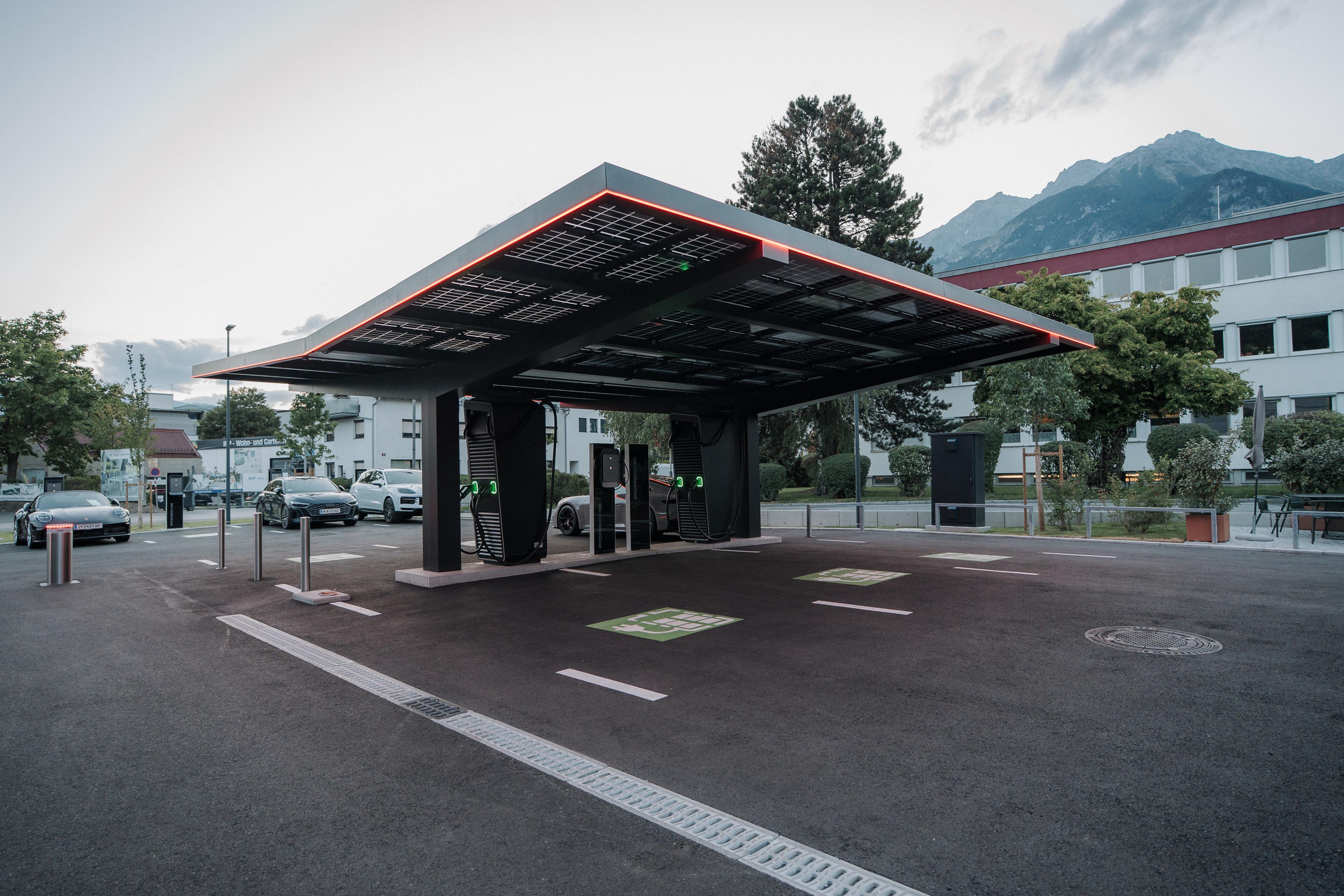 Modern electric vehicle charging station with a covered roof, surrounded by trees and mountains in the background.