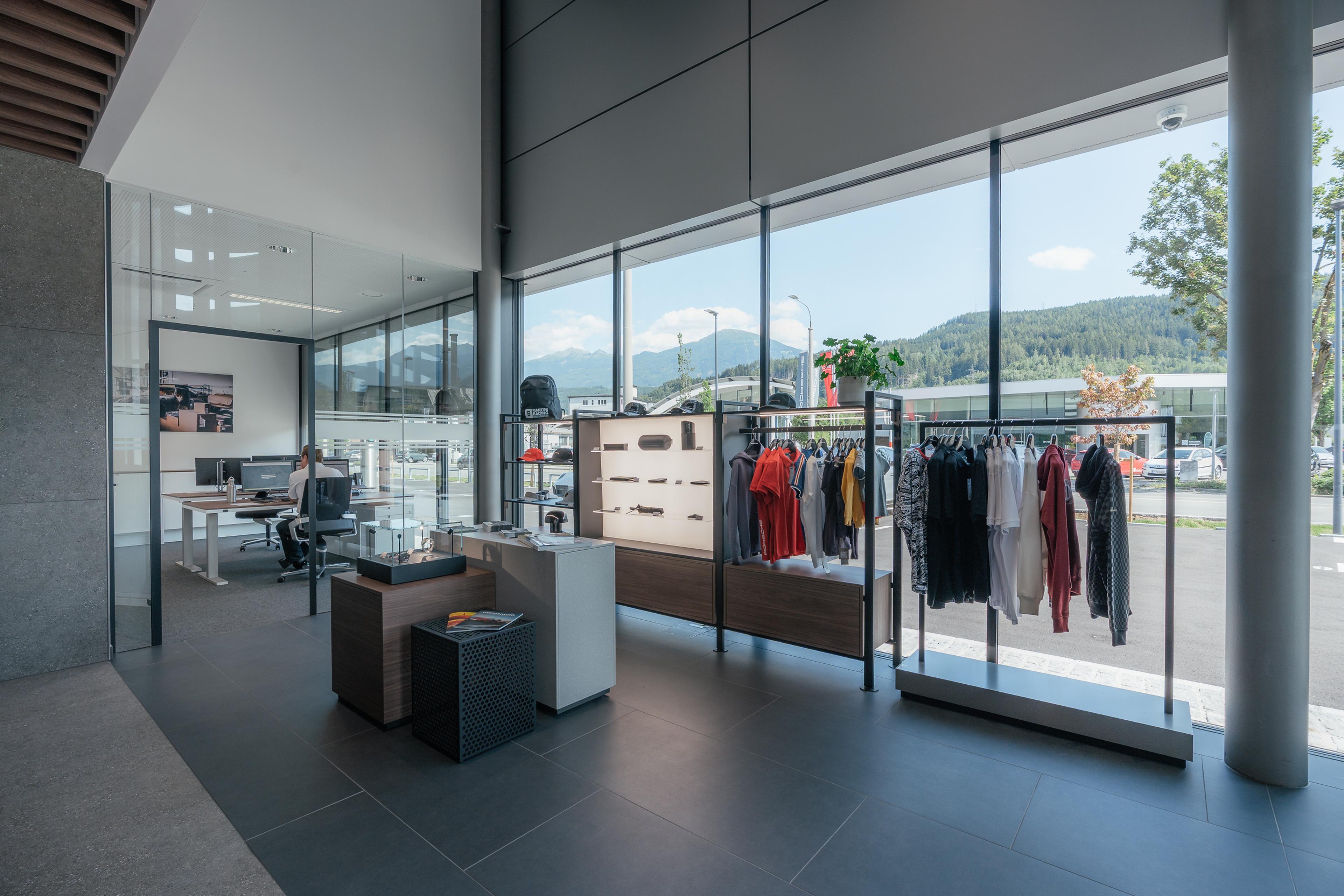 Modern showroom with glass walls displaying clothing and accessories. Outdoor view of trees and mountains visible through large windows.