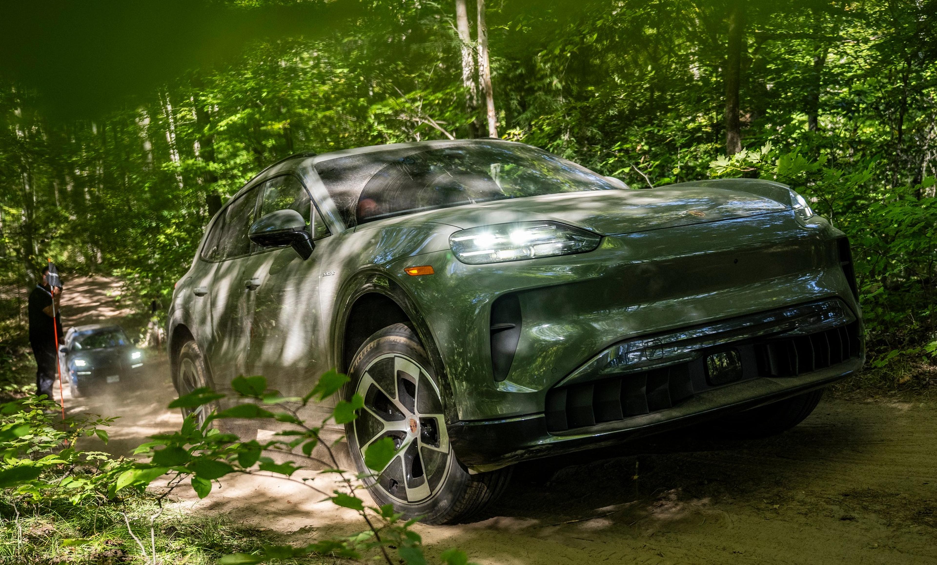 Two Porsche Cayenne's drive through a dense forest on a dirt trail, surrounded by lush green trees and vegetation.