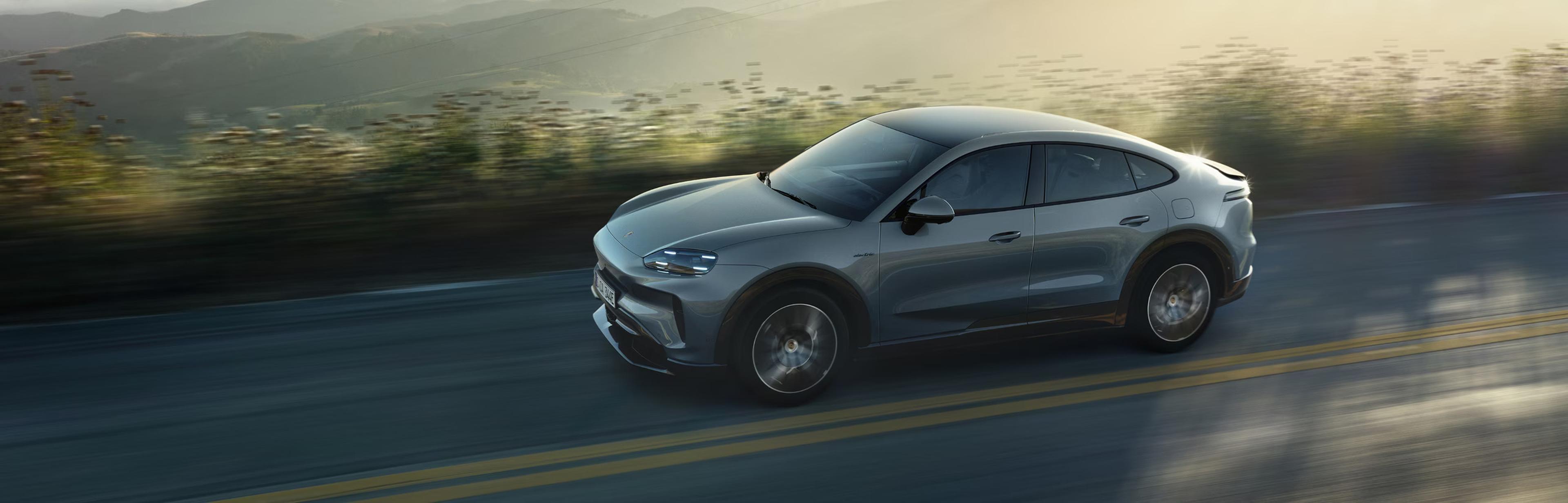 The 2027 Porsche Cayenne Coupe Electric driving on a road with a valley view in the background