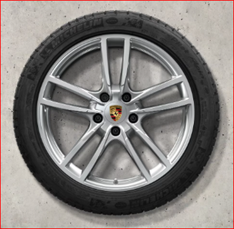 A silver alloy Cayenne wheel with a Porsche emblem, mounted with a black Michelin tire, against a concrete background.