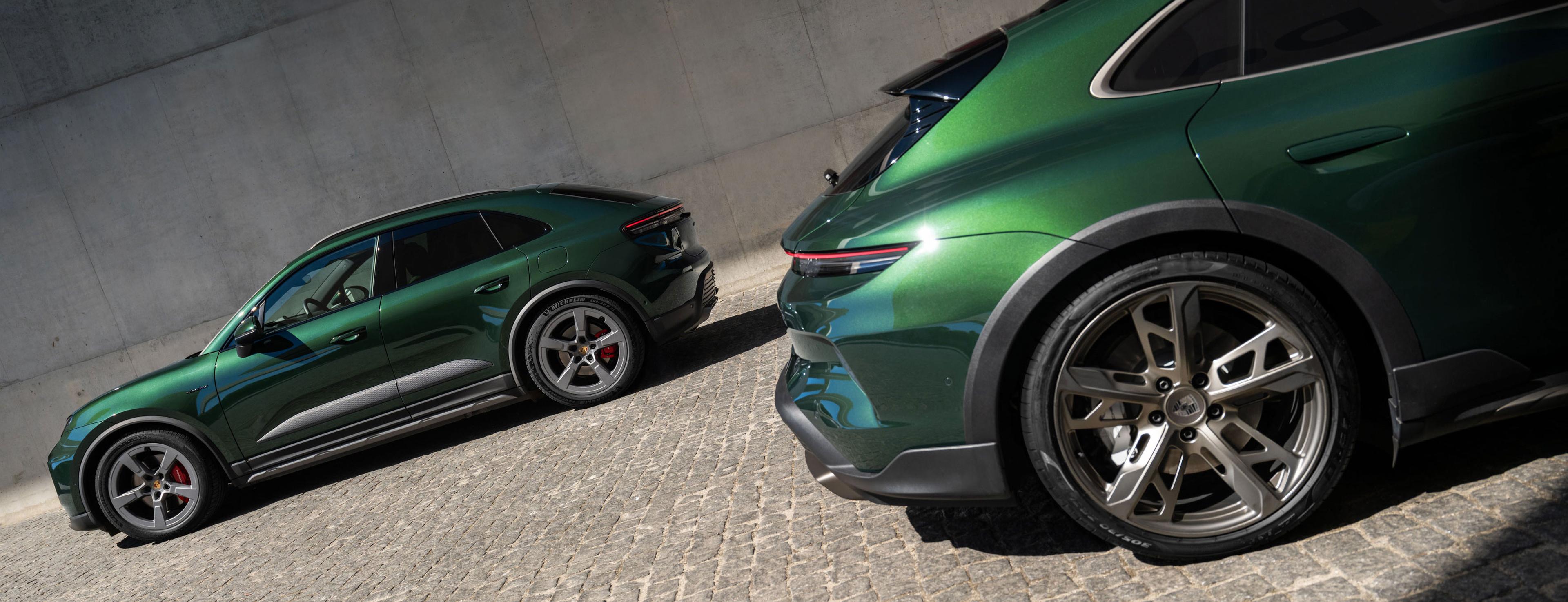 Zwei grüne Porsche Sportwagen parken auf einer Kopfsteinpflasterstraße; sie stehen schräg zueinander und präsentieren ihr elegantes Design sowie ihre Leichtmetallfelgen.