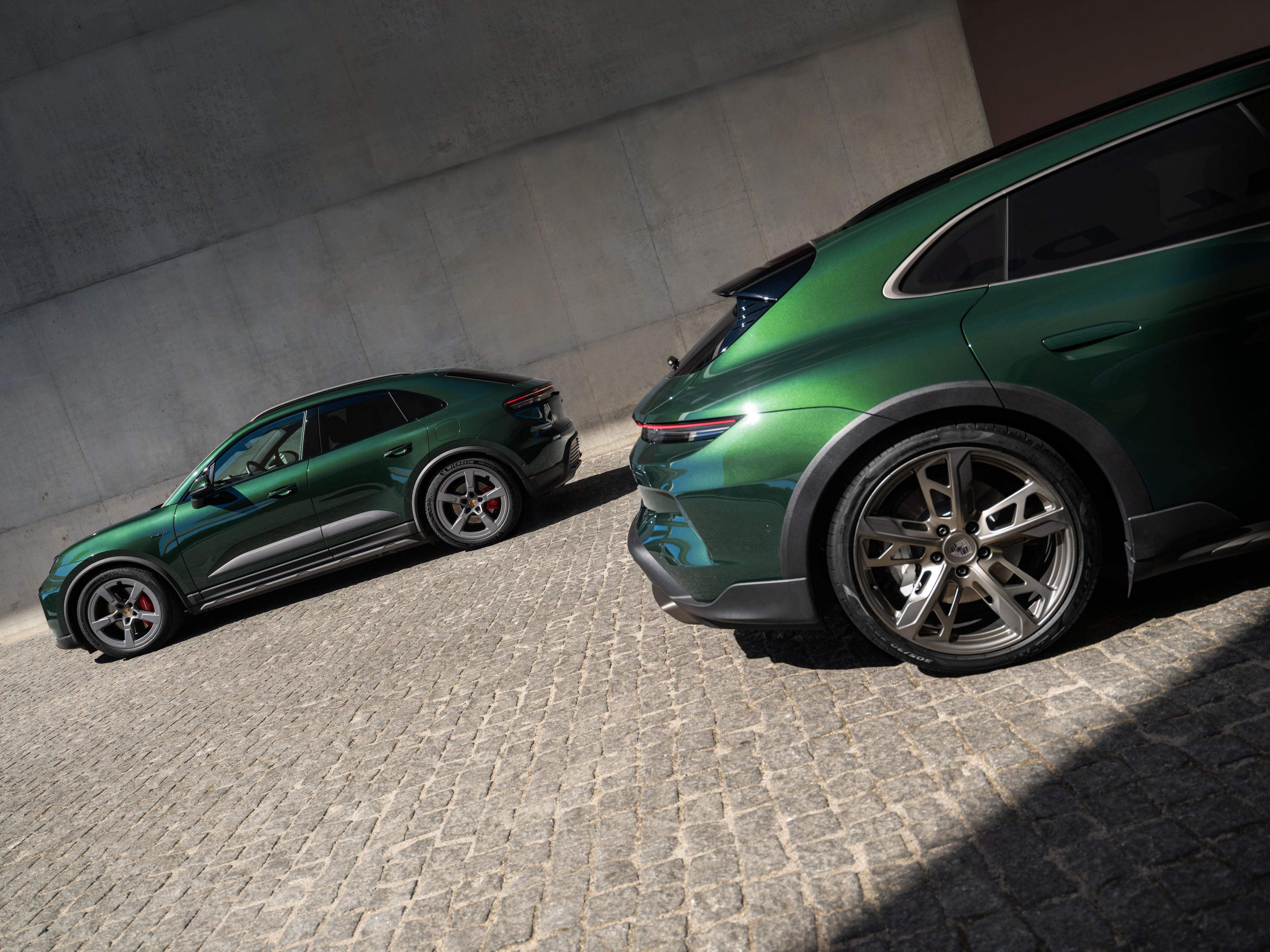 Zwei grüne Sportwagen parken auf einer Kopfsteinpflasterstraße; sie stehen schräg zueinander und präsentieren ihr elegantes Design sowie ihre Leichtmetallfelgen.