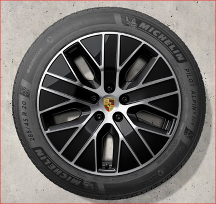 Black and silver alloy Porsche Macan Electric wheel with a Porsche logo, fitted with a Michelin Pilot Alpin SUV tire on a concrete surface.