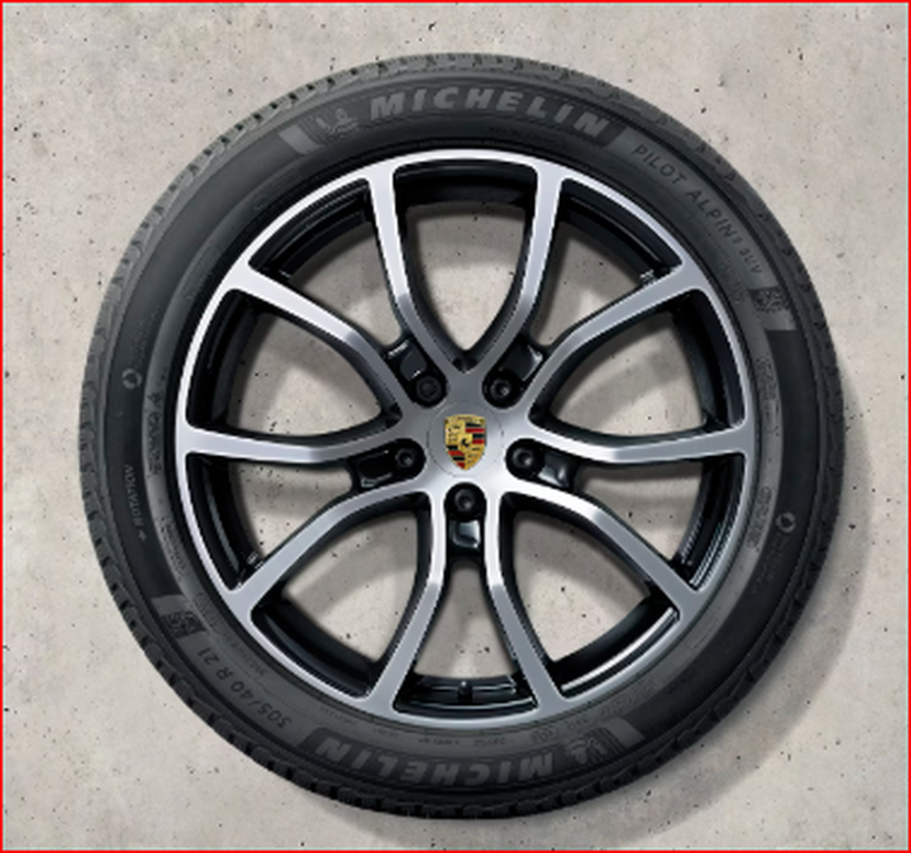 A Cayenne black and silver alloy wheel with a Michelin tire, featuring a Porsche logo at the center, on a concrete background.