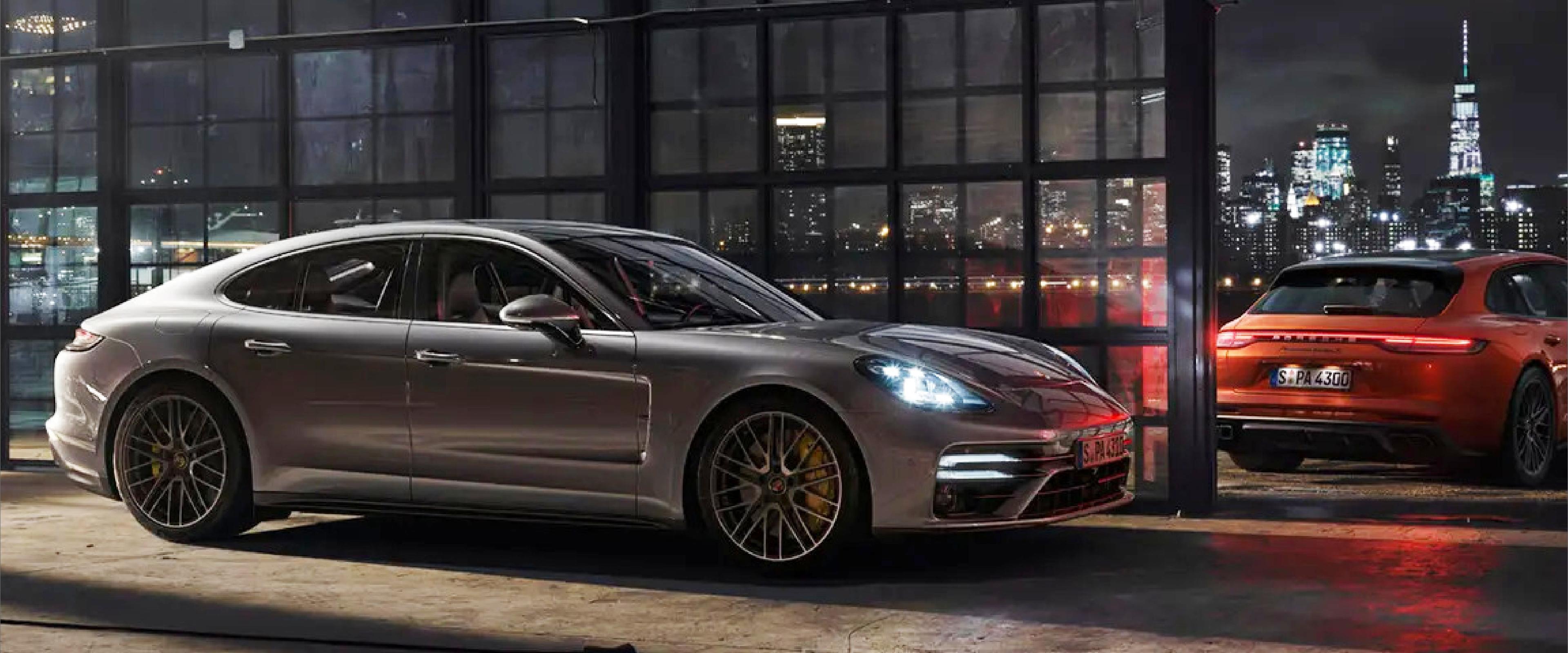 two_porsche_panameras_parked_against_glass_wall_with_cityscape_in_the_background