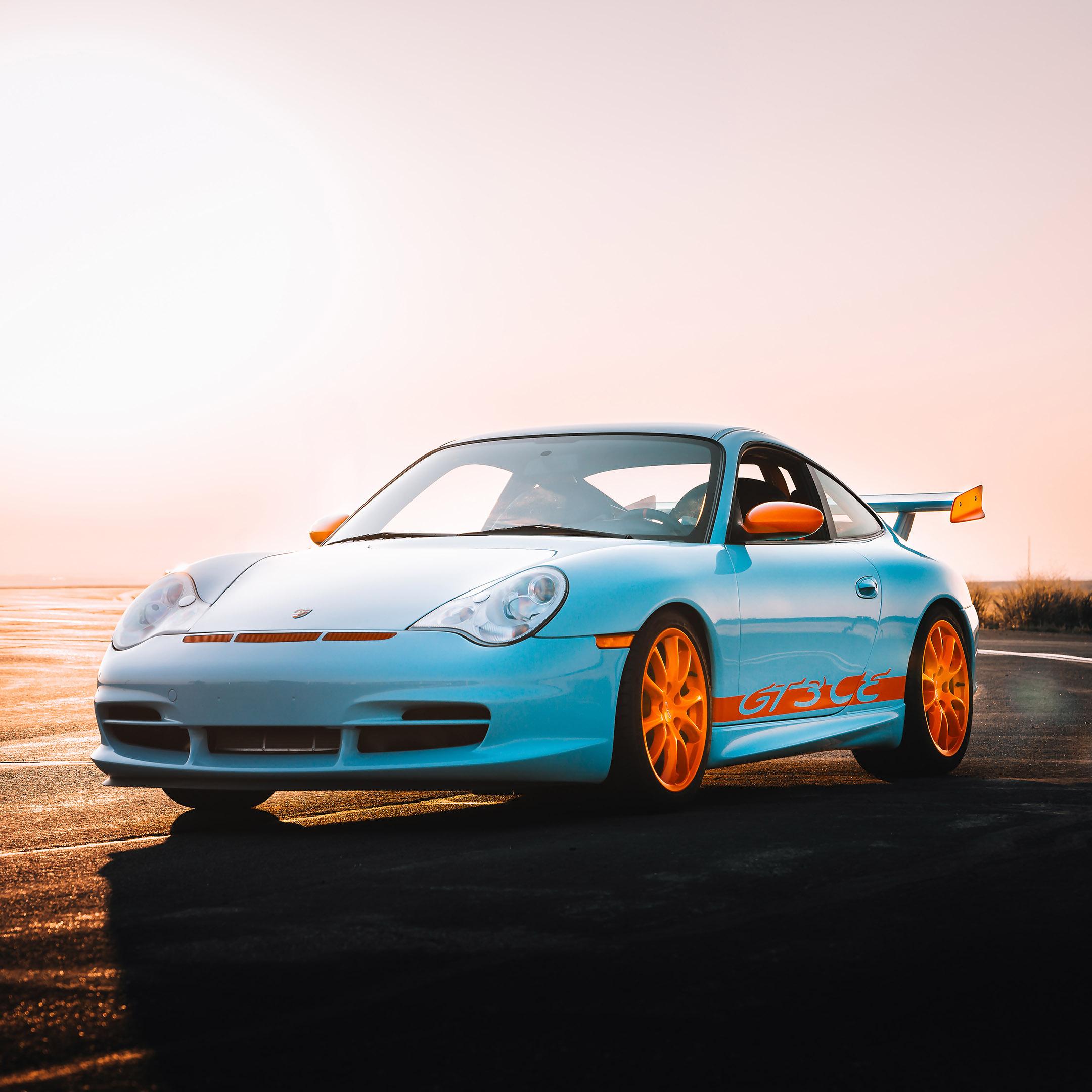 A blue sports car with orange rims and accents on a winding road at sunset.