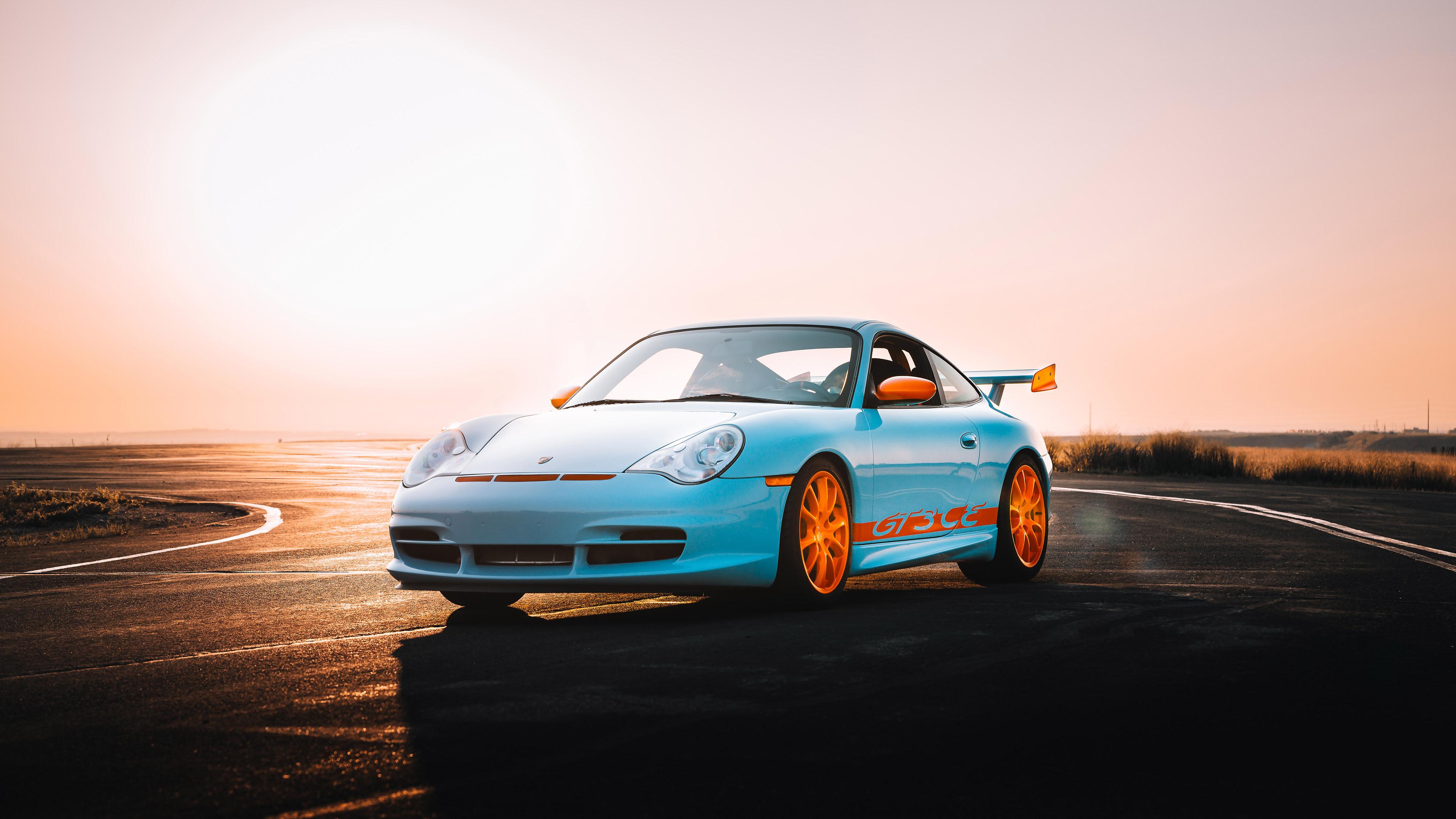 A blue sports car with orange rims and accents on a winding road at sunset.