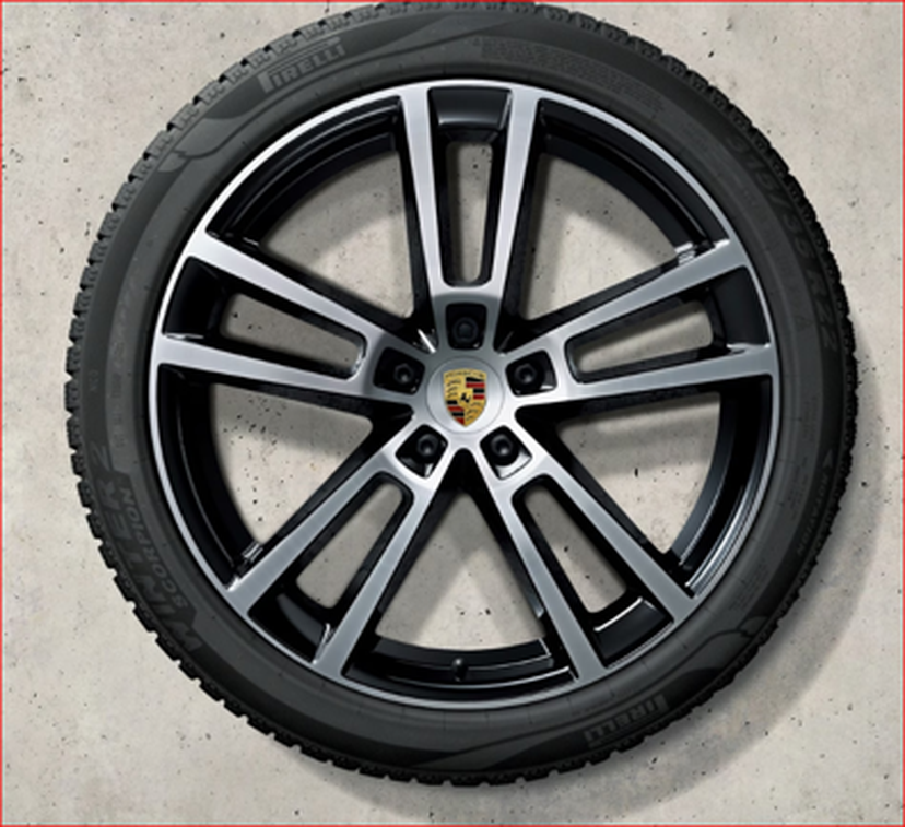 Cayenne Black and silver alloy wheel with a Porsche logo, featuring a five-spoke design, lying on a smooth concrete surface.