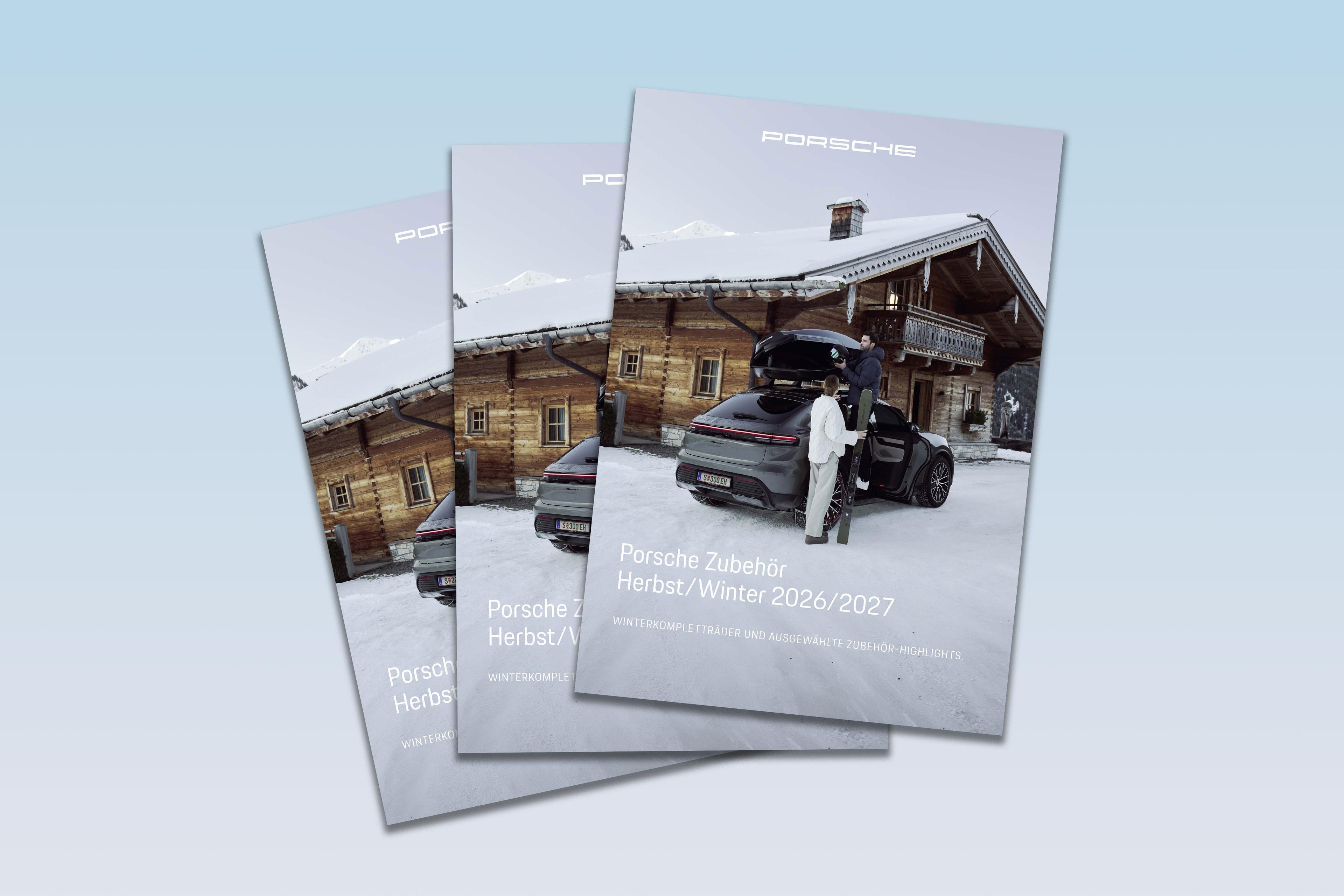 Drei Broschüren, die einen Porsche vor einer verschneiten Hütte zeigen und Herbst-/Winter-Accessoires für 2026/2027 bewerben.