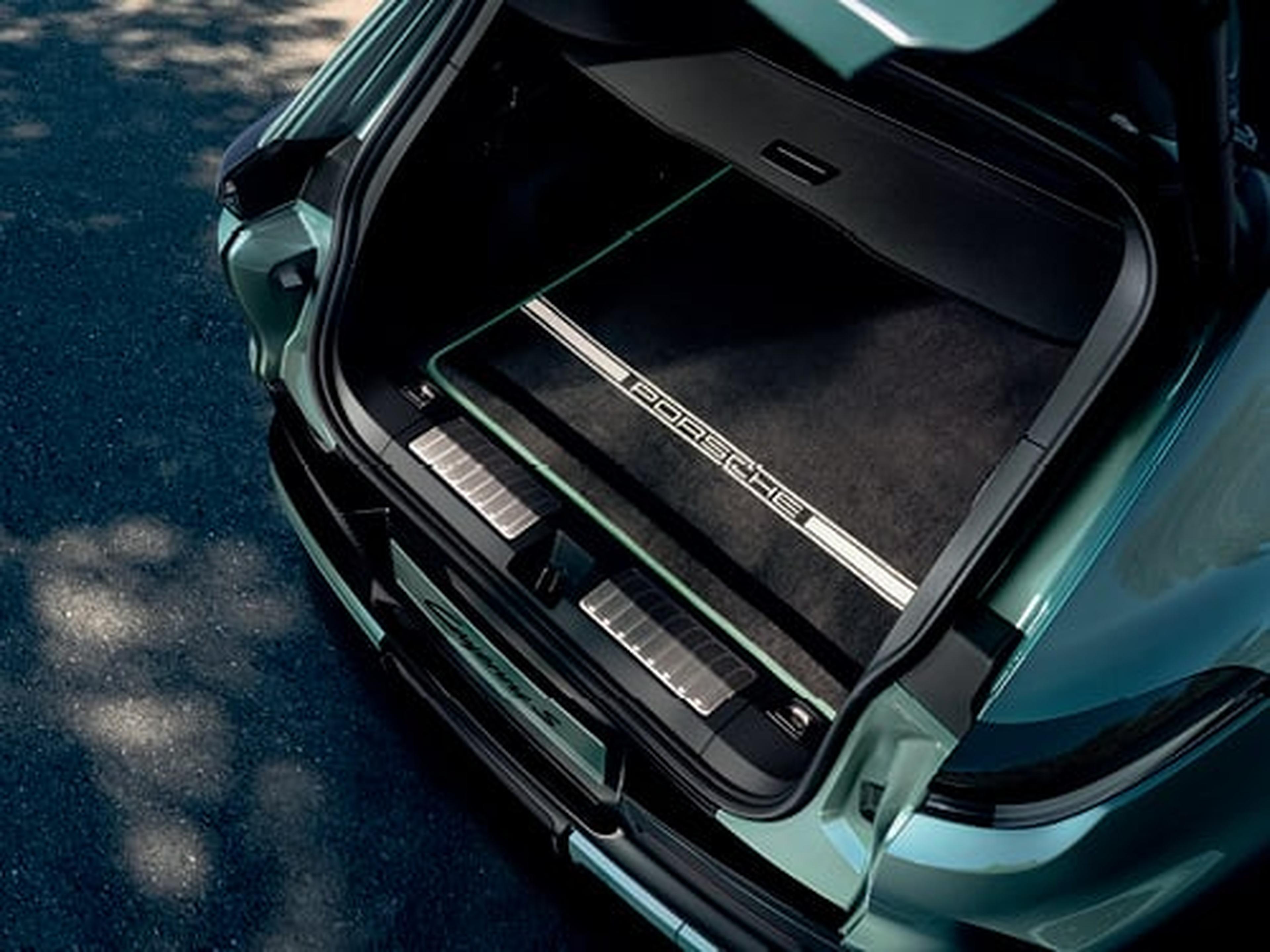 Detalle del maletero abierto de un Porsche Macan verde, revelando una alfombra protectora negra con el icónico logo "PORSCHE" y líneas deportivas.