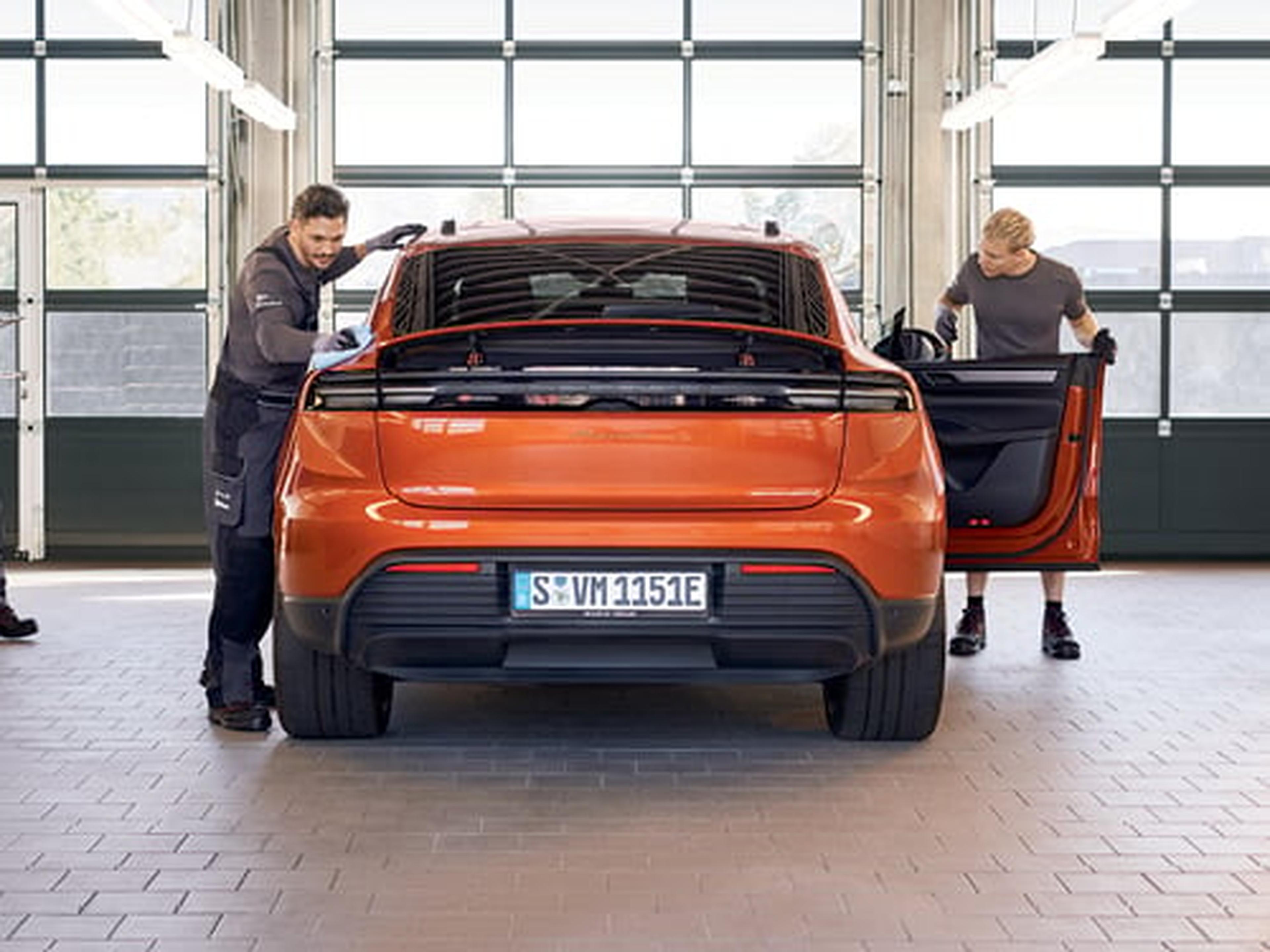 Técnicos revisando la parte trasera de un Porsche Taycan Cross Turismo naranja en un taller, con puertas abiertas.