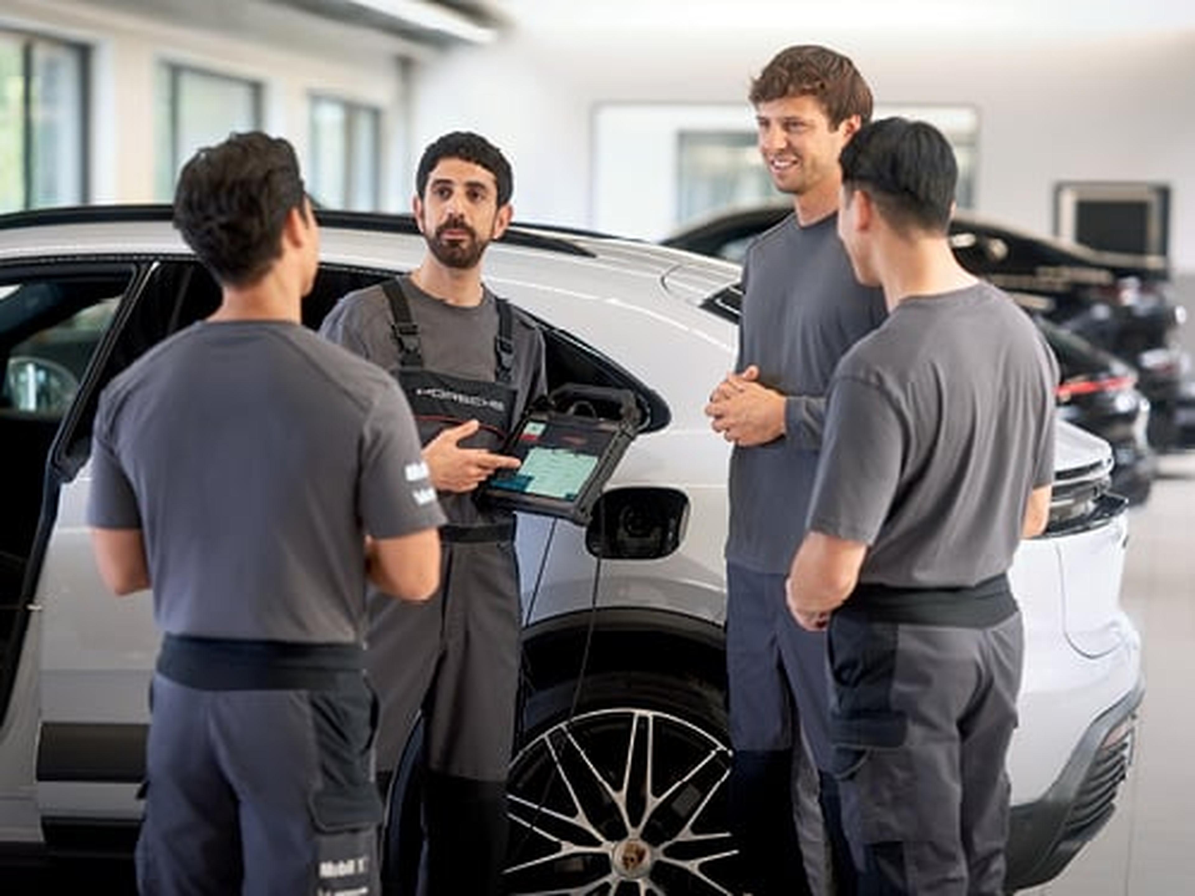 Grupo de técnicos de Porsche discutiendo frente a un Porsche Taycan blanco en un taller.