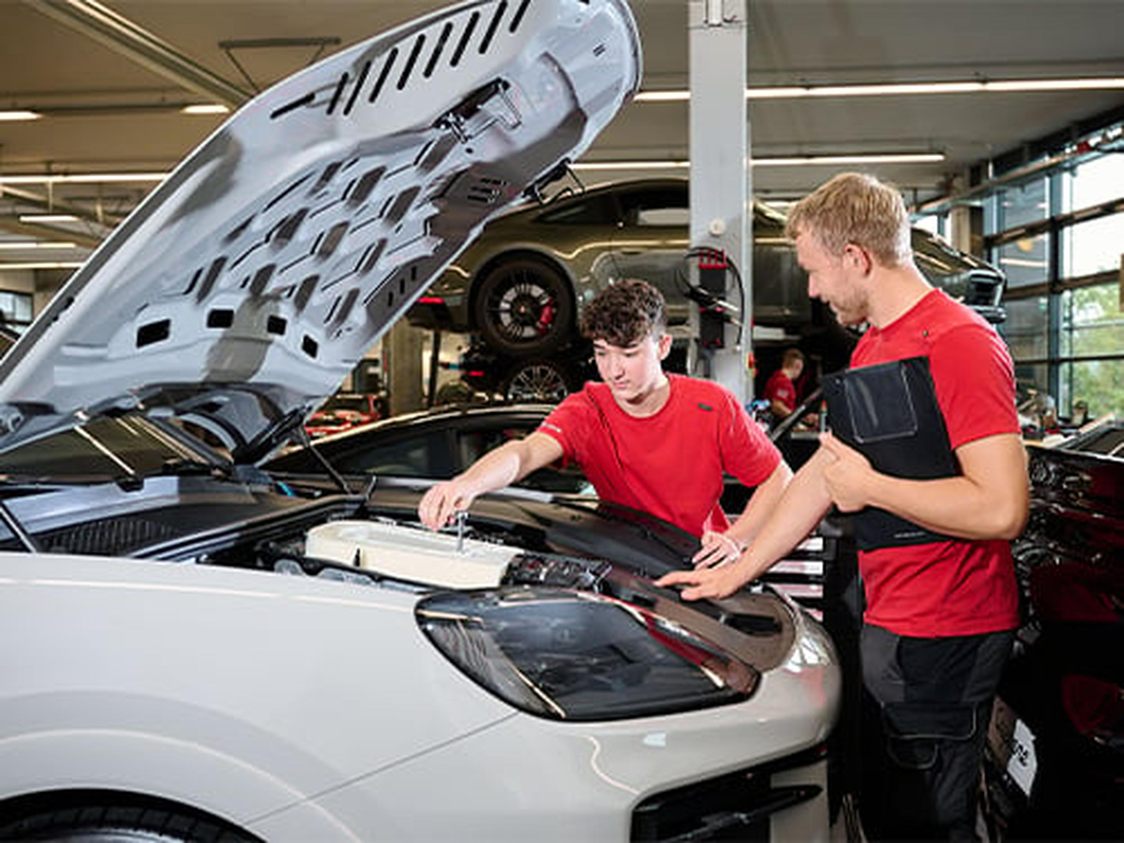 Zwei Porsche Werkstattmitarbeiter überprüfen einen Porsche Sportwagen.