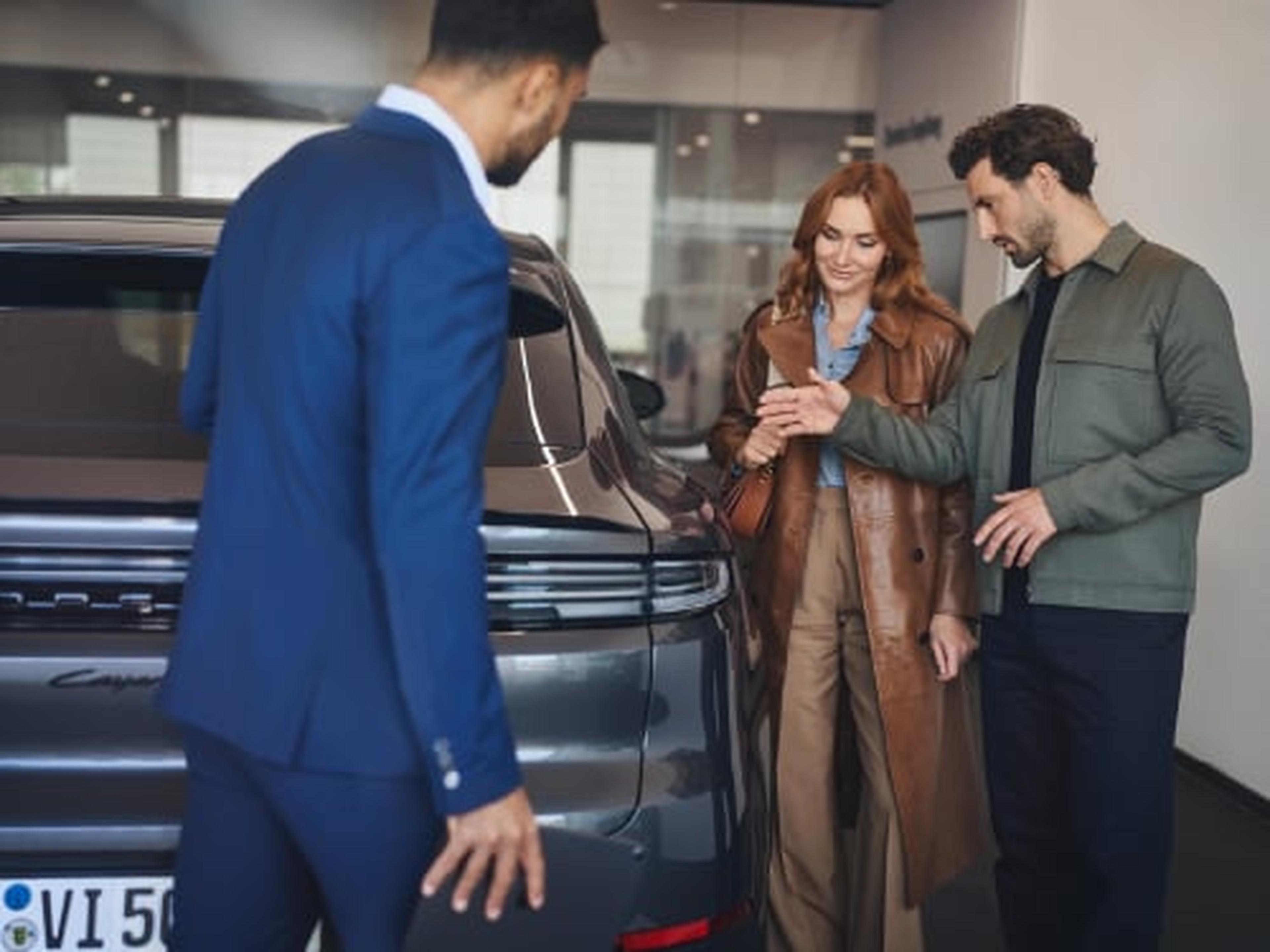 pareja y vendedor en concesionario viendo un porsche cayenne