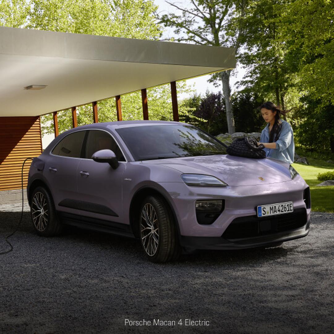 Three-quarter front view of a Porsche Macan 4 Electric in Purple charging in a lush backyard setting.