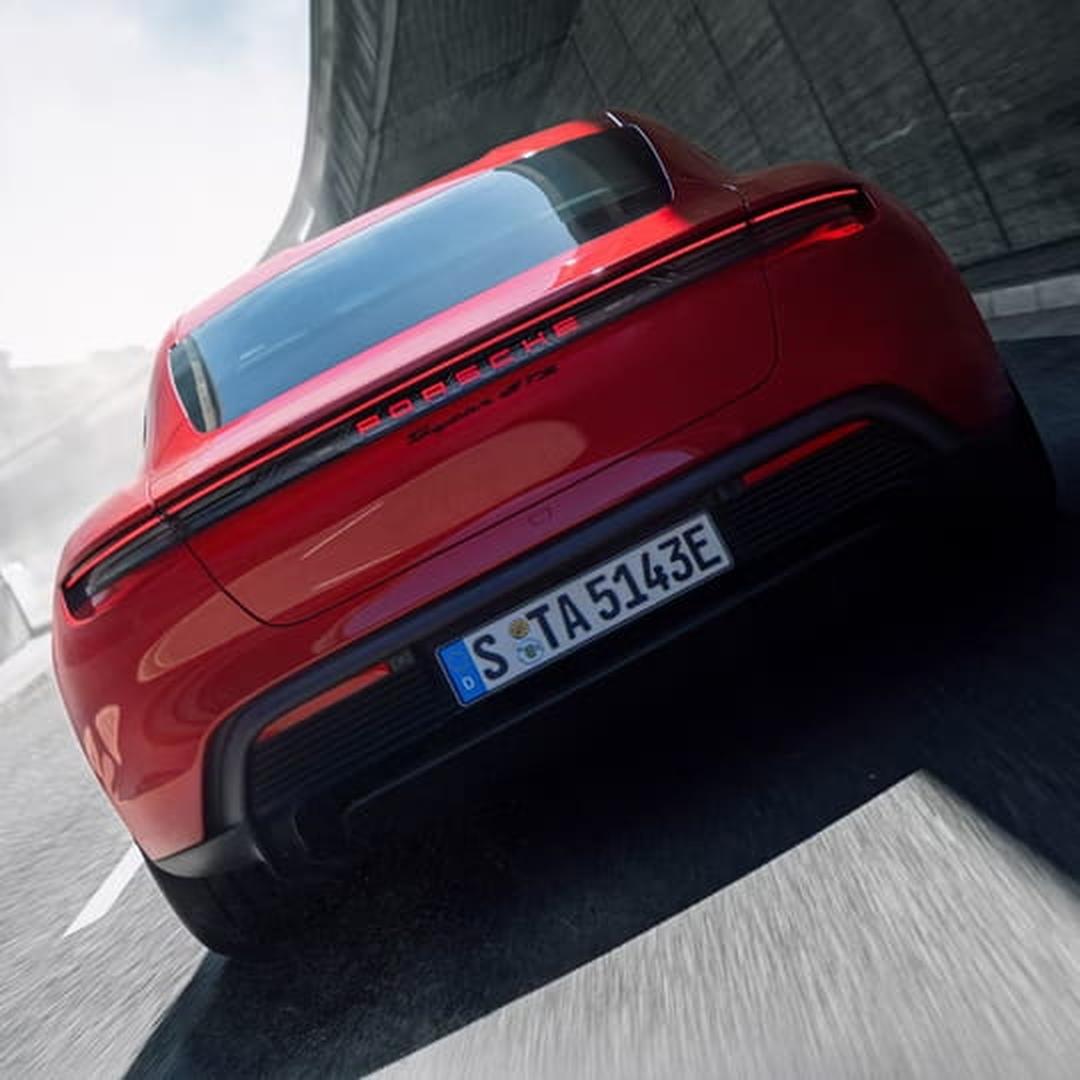 Red Porsche Taycan shown from a low rear angle while driving on a curved road.