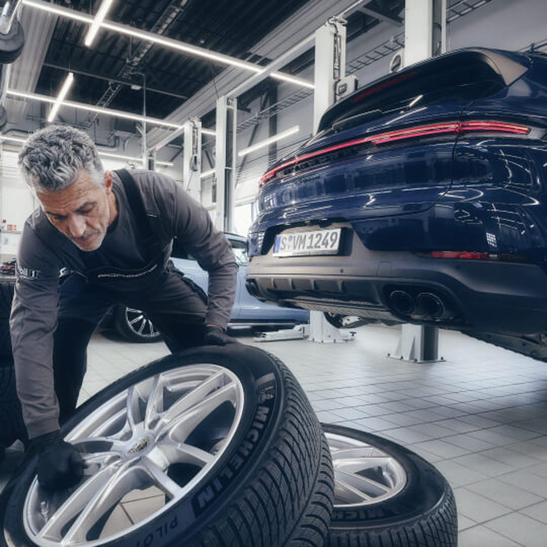 Low-angle view of a Porsche Cayenne S in Blue with a service technician aligning a tire.