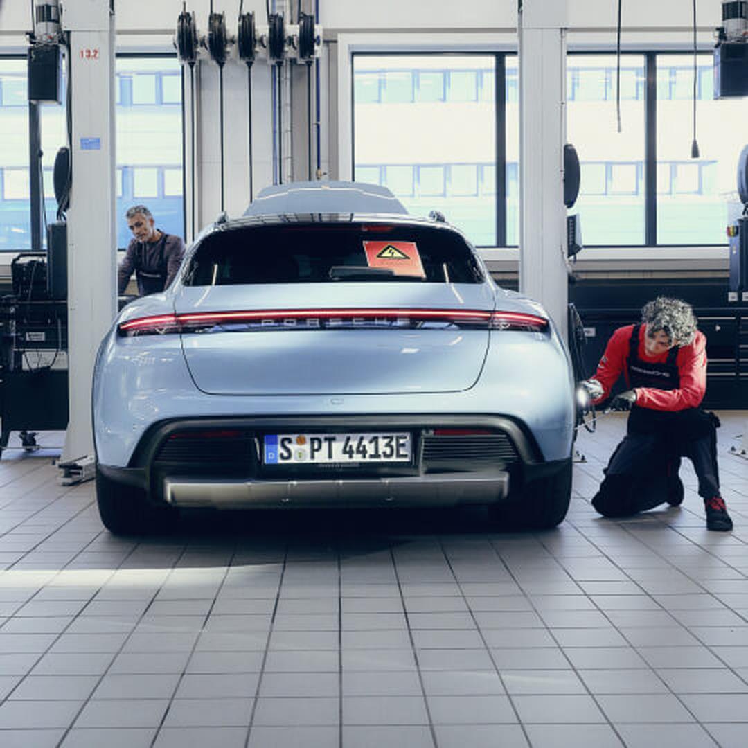 Rear view of a Porsche Taycan Cross Turismo in Blue with a kneeling mechanic holding a tool.