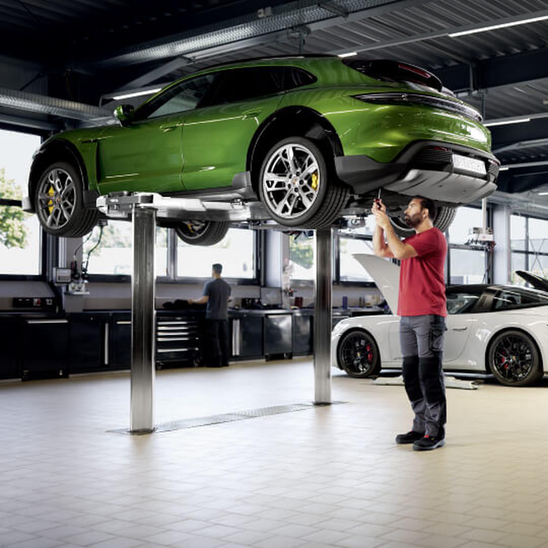 Low-angle view of a Porsche Taycan Cross Turismo in Green with a technician inspecting the undercarriage.