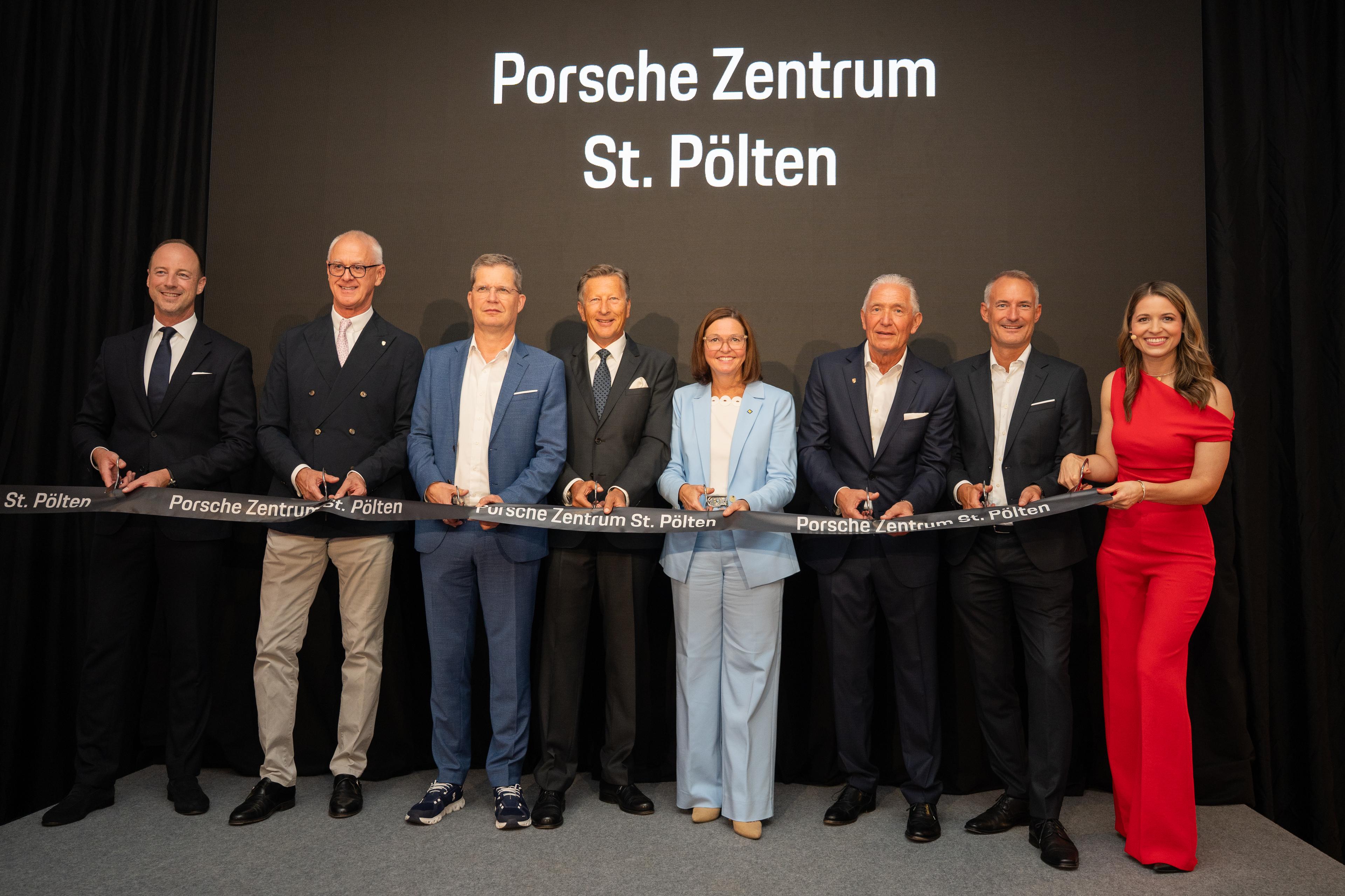 Auf der Bühne im eleganten Porsche Showroom stehen mehrere Führungspersönlichkeiten und Ehrengäste gemeinsam nebeneinander und durchschneiden symbolisch ein schwarzes Eröffnungsband mit mehreren Schere.