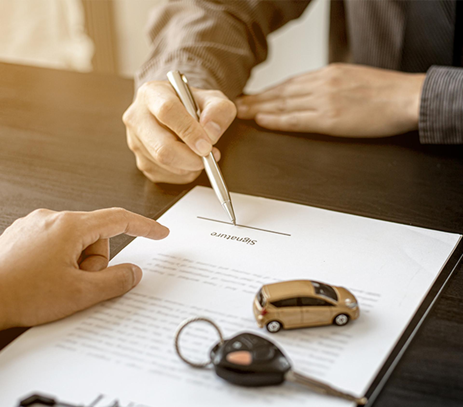 Person signing car purchase agreement with keys and toy car on desk