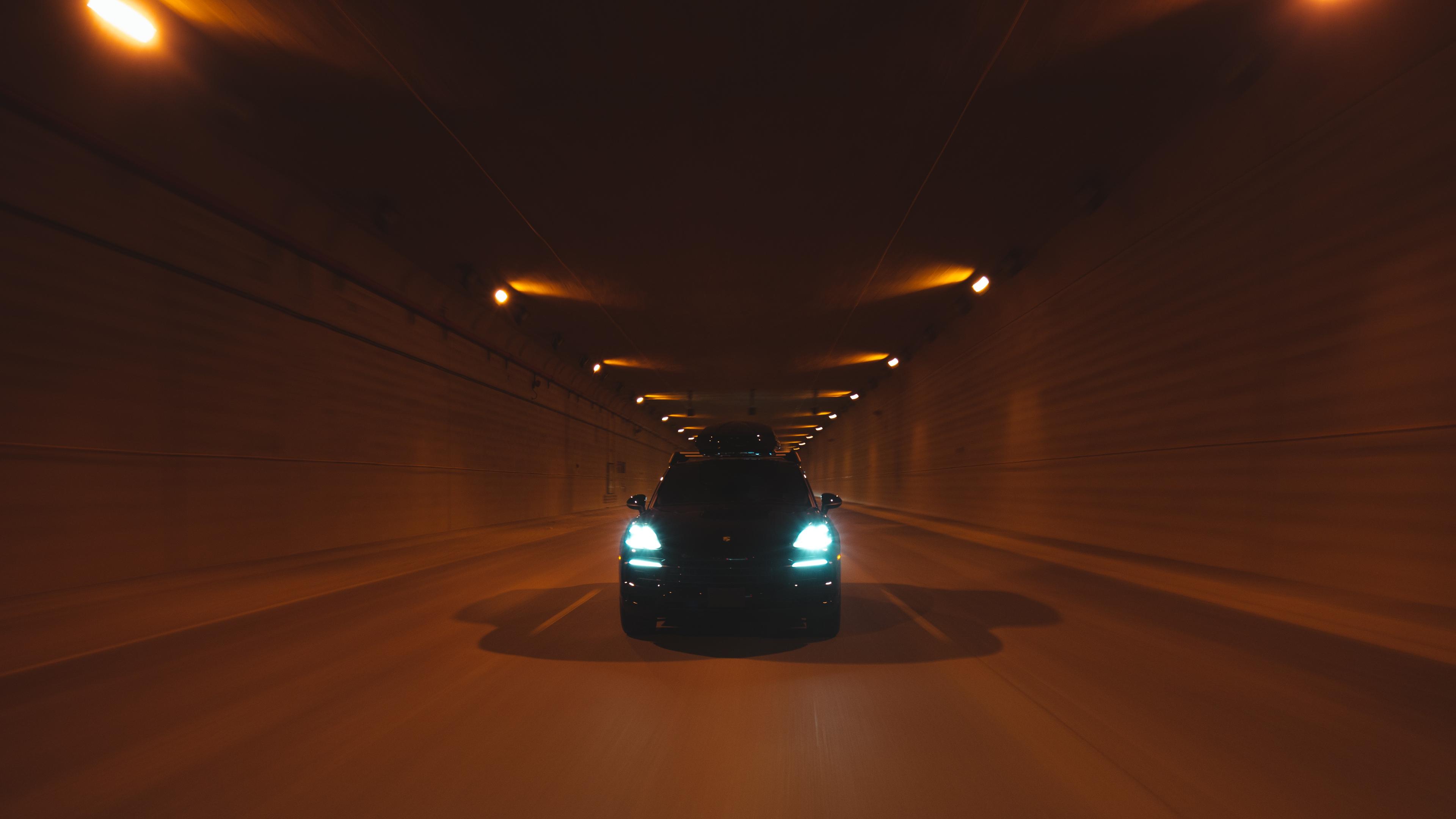 Cayenne Tequipment with bright headlights driving through a dimly lit tunnel, casting shadows on the road.