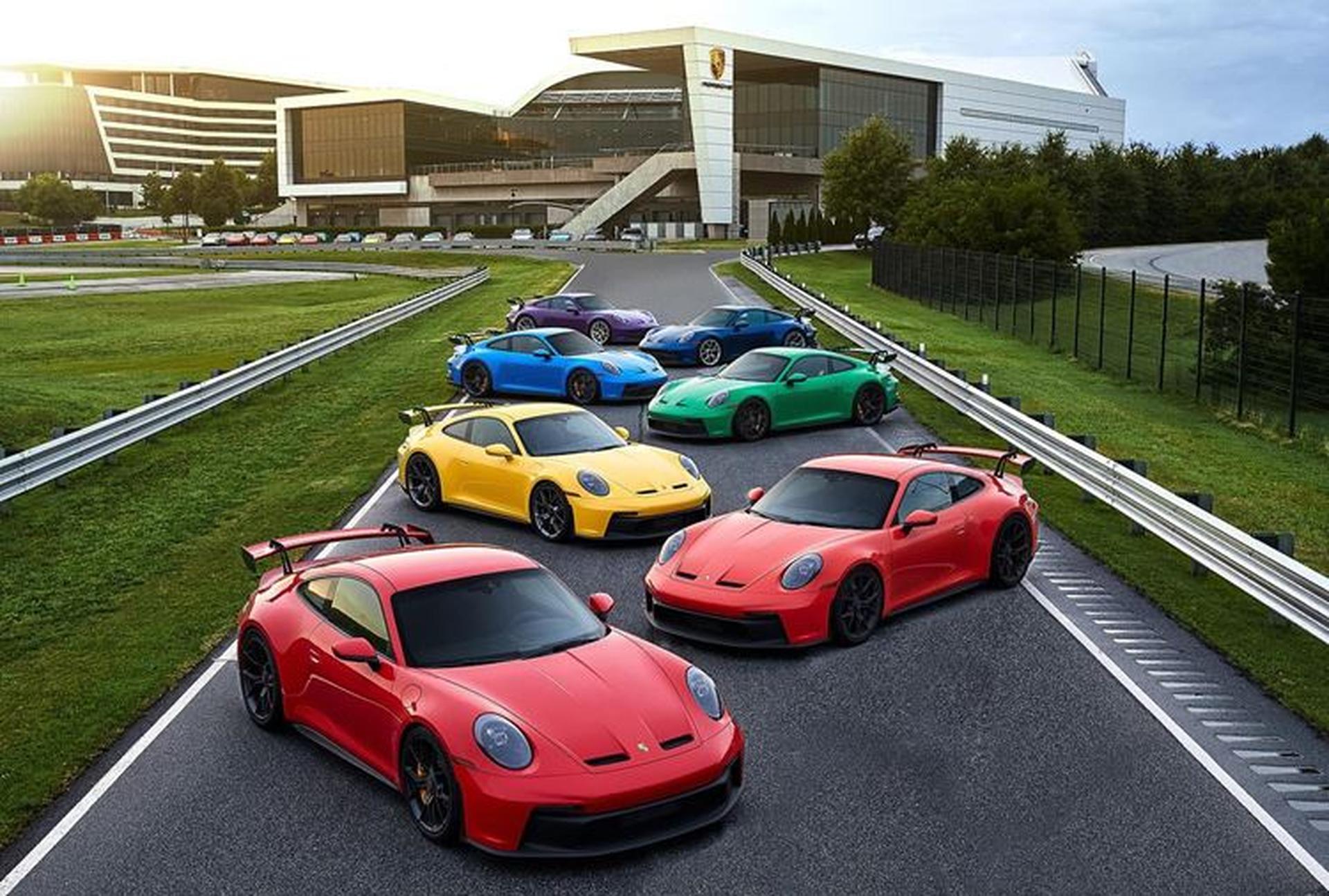Six colorful 911 GT3 sports cars parked on the racetrack at Porsche Experience Center Atlanta, with lush greenery surrounding the scene.