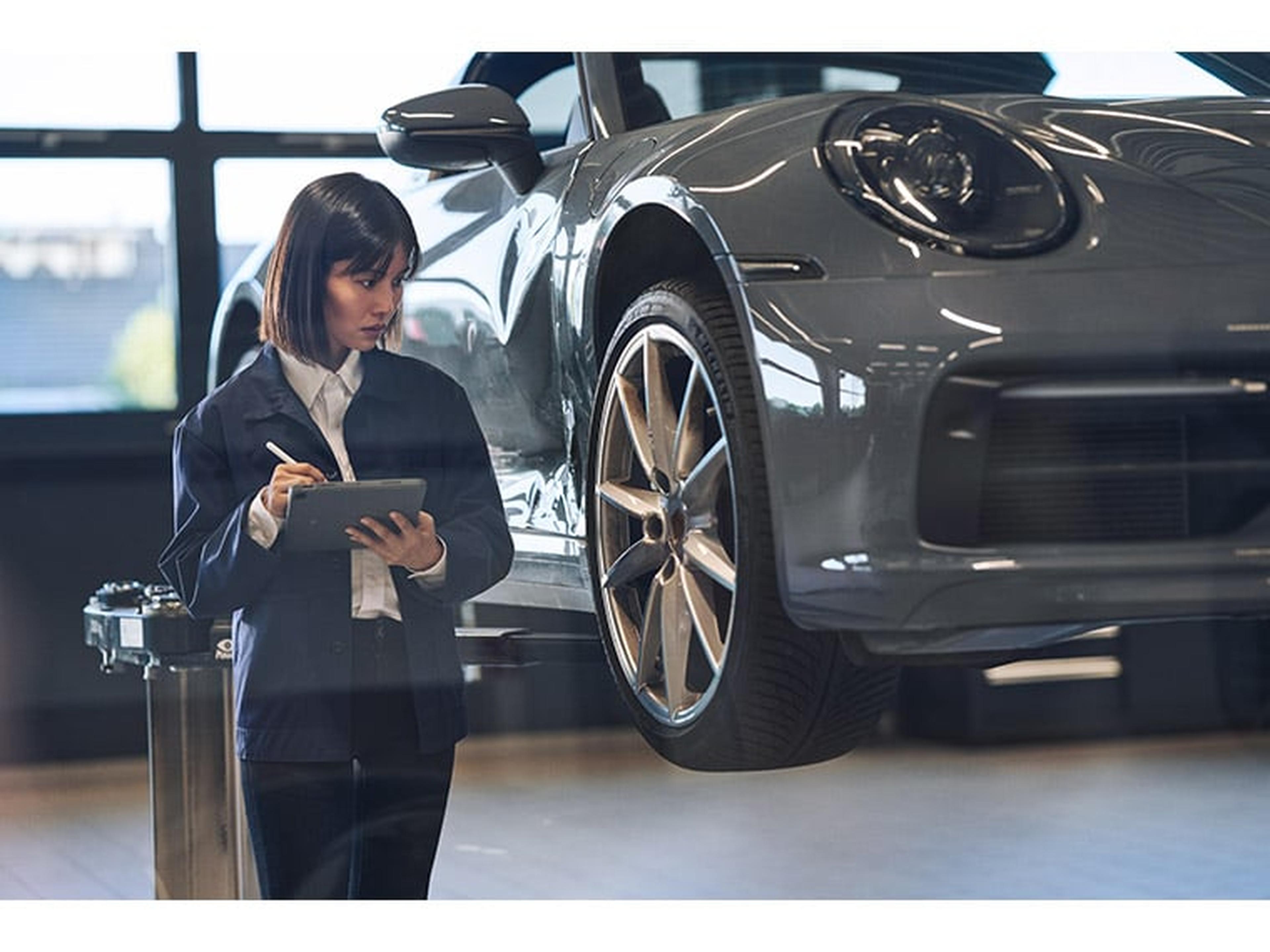 Eine Technikerin inspiziert einen Porsche auf einem Wagenheber