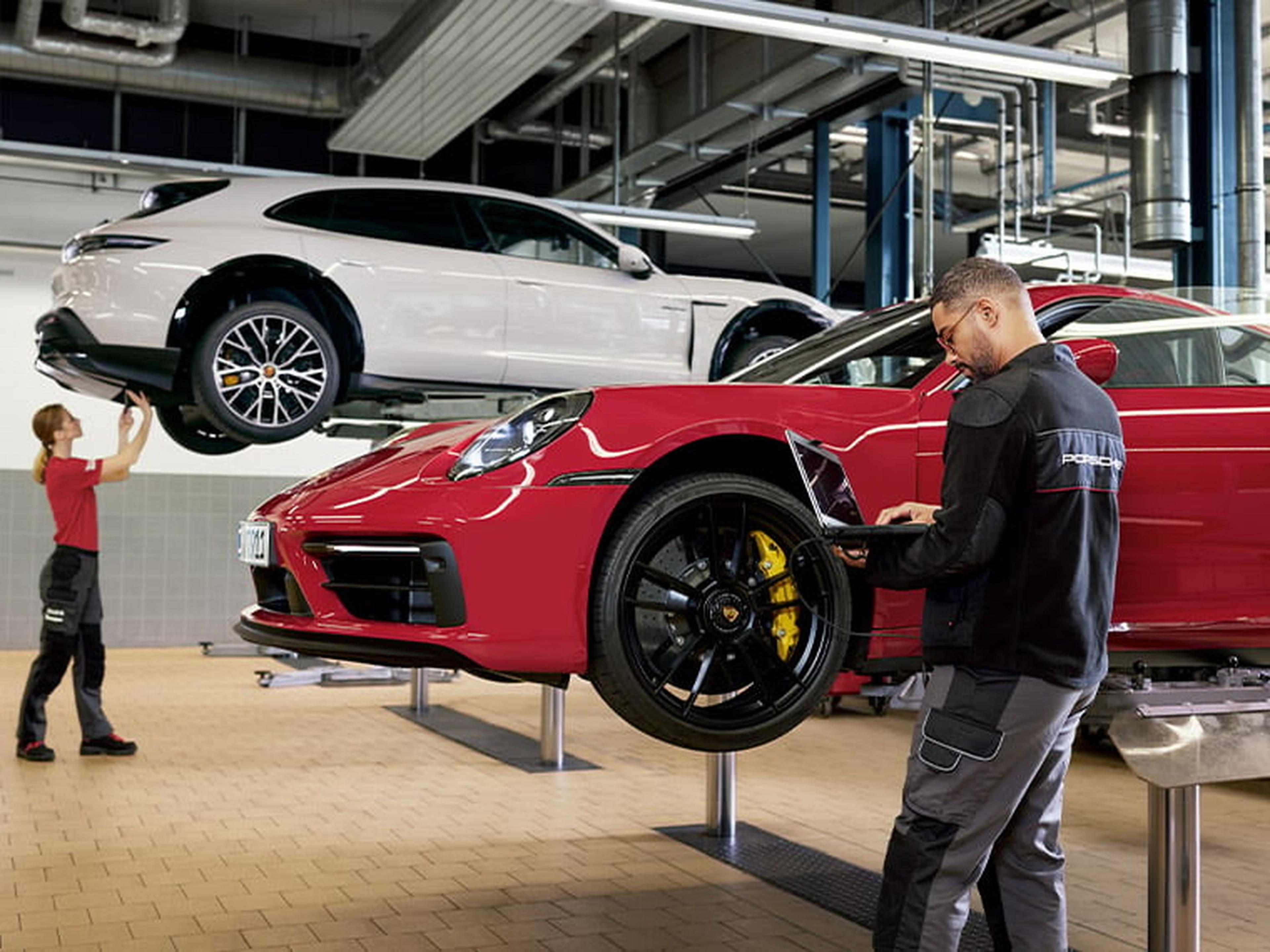 Zwei Porsche werden in einer Werkstatt inspiziert, der hintere steht auf einer Hebebühne