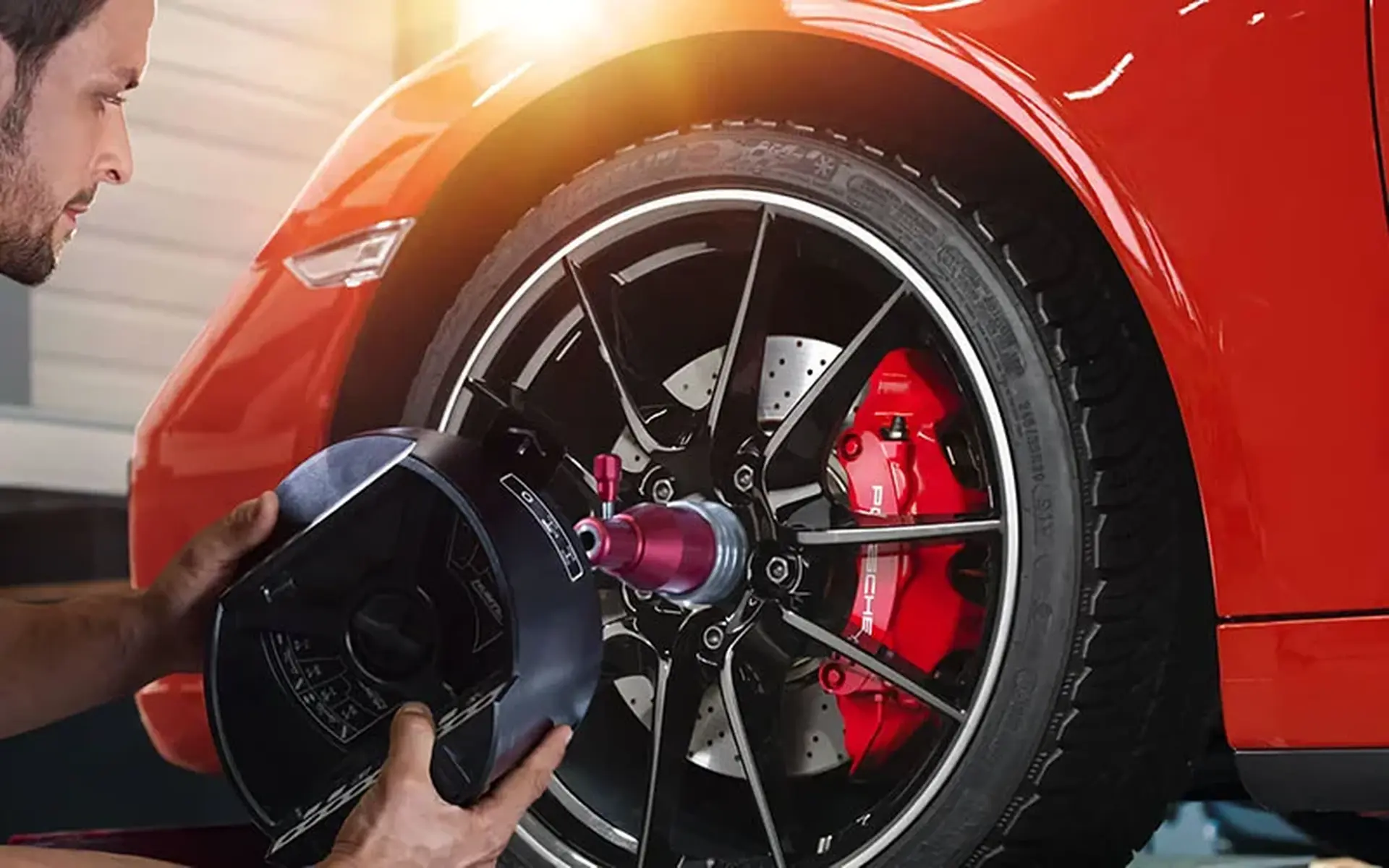 A mechanic polishes a red car's wheel with a buffing tool, revealing a bright, shiny brake caliper beneath.