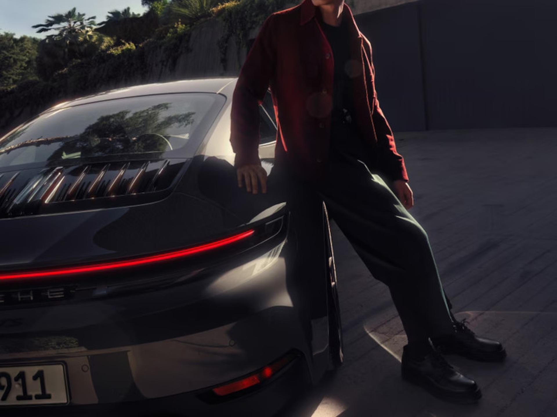 Person leaning on a sleek, modern car with a bright red taillight, set in a dimly lit urban environment.