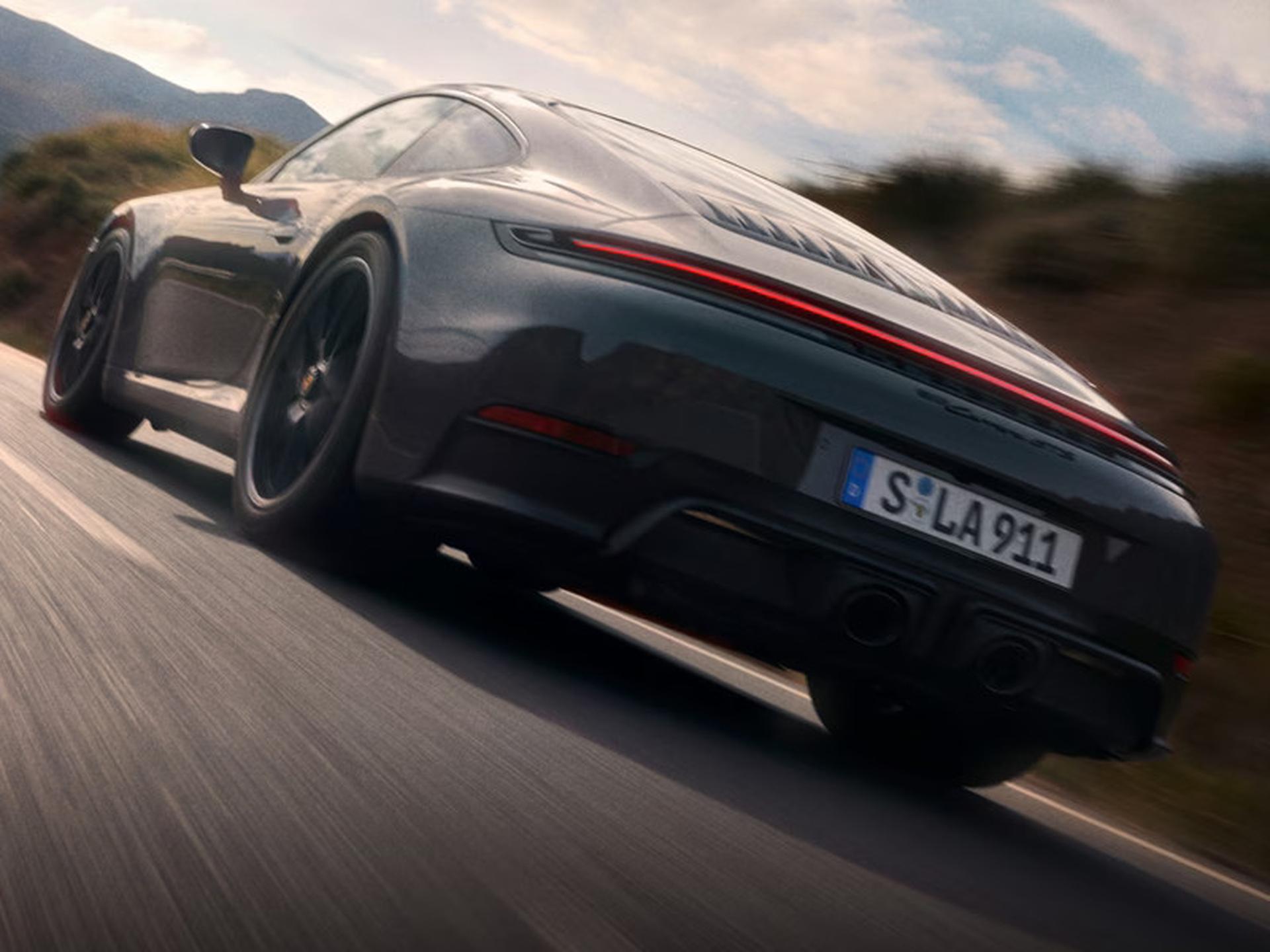 Sleek black sports car driving on a scenic mountain road with a blurred background, showcasing its dynamic motion.