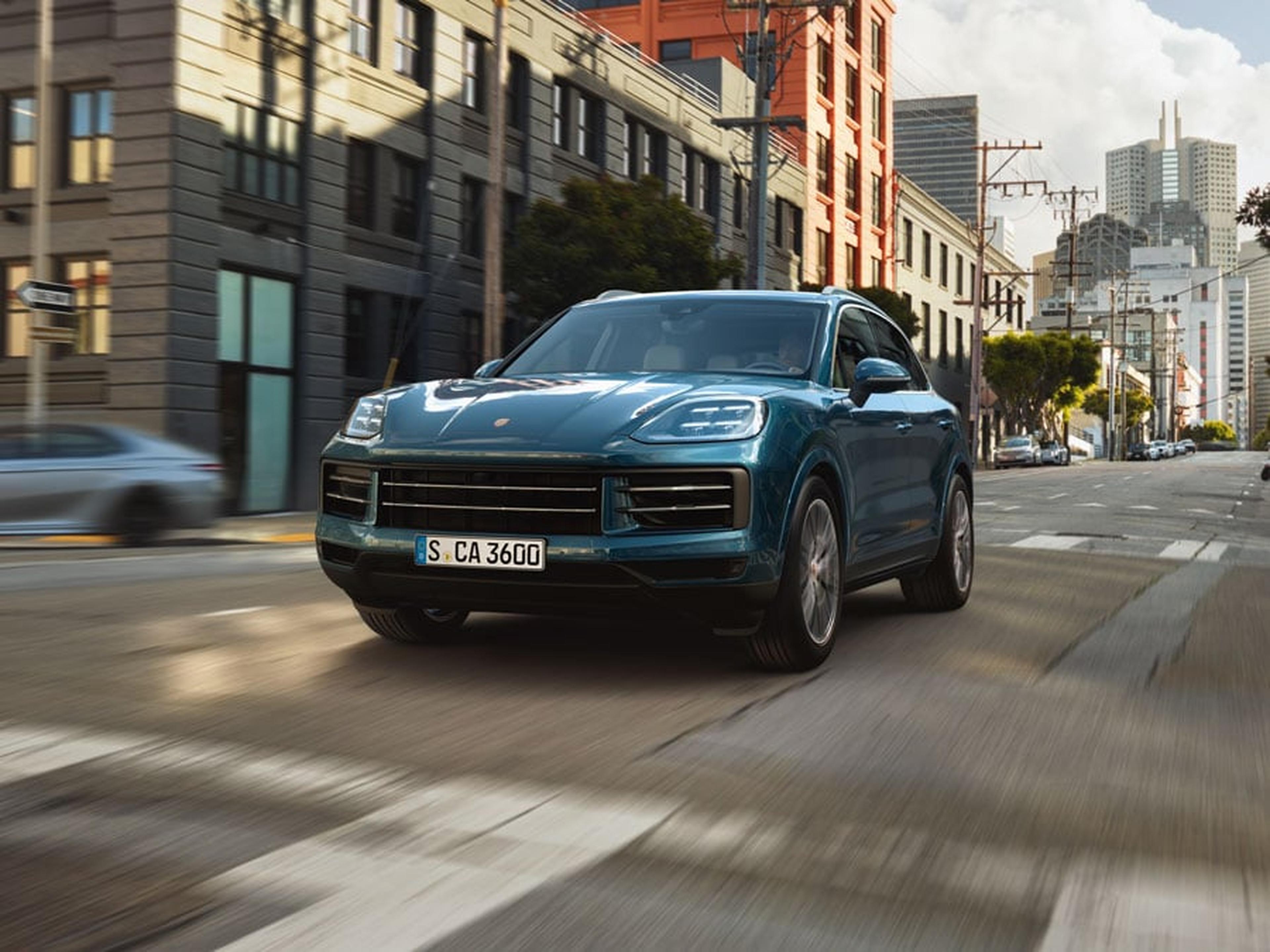 A blue Porsche Cayenne drives through a city street.