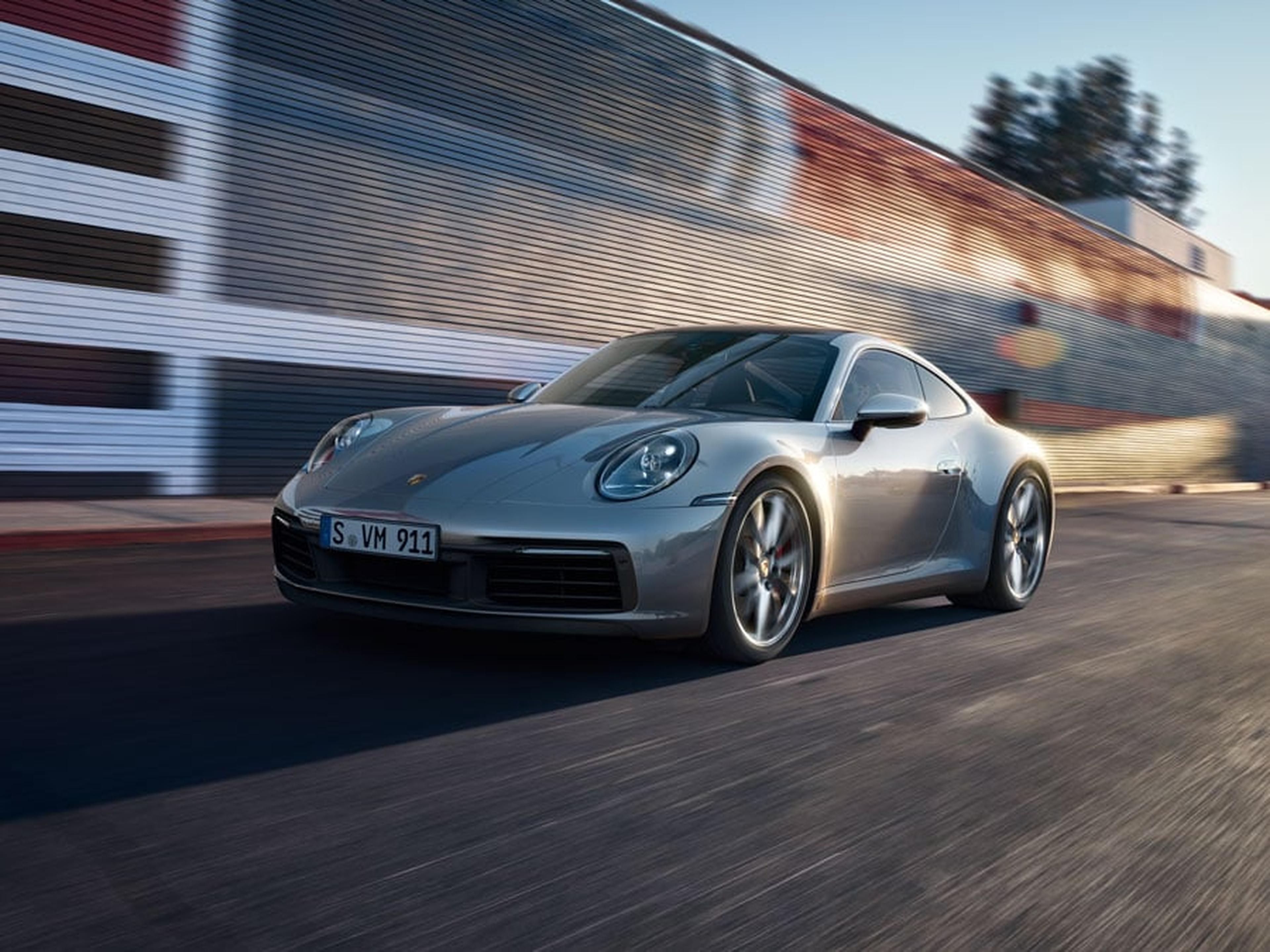 A silver Porsche 911 drives along a road.