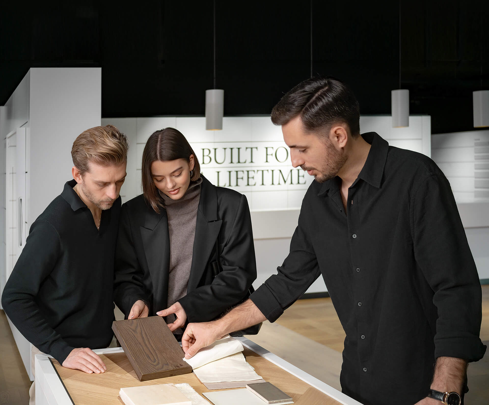 Ein Berater zeigt einem jungen Paar verschiedene Parkett‑ und Holzmustertafeln in einem modernen Showroom, während sie gemeinsam Farboptionen vergleichen. 