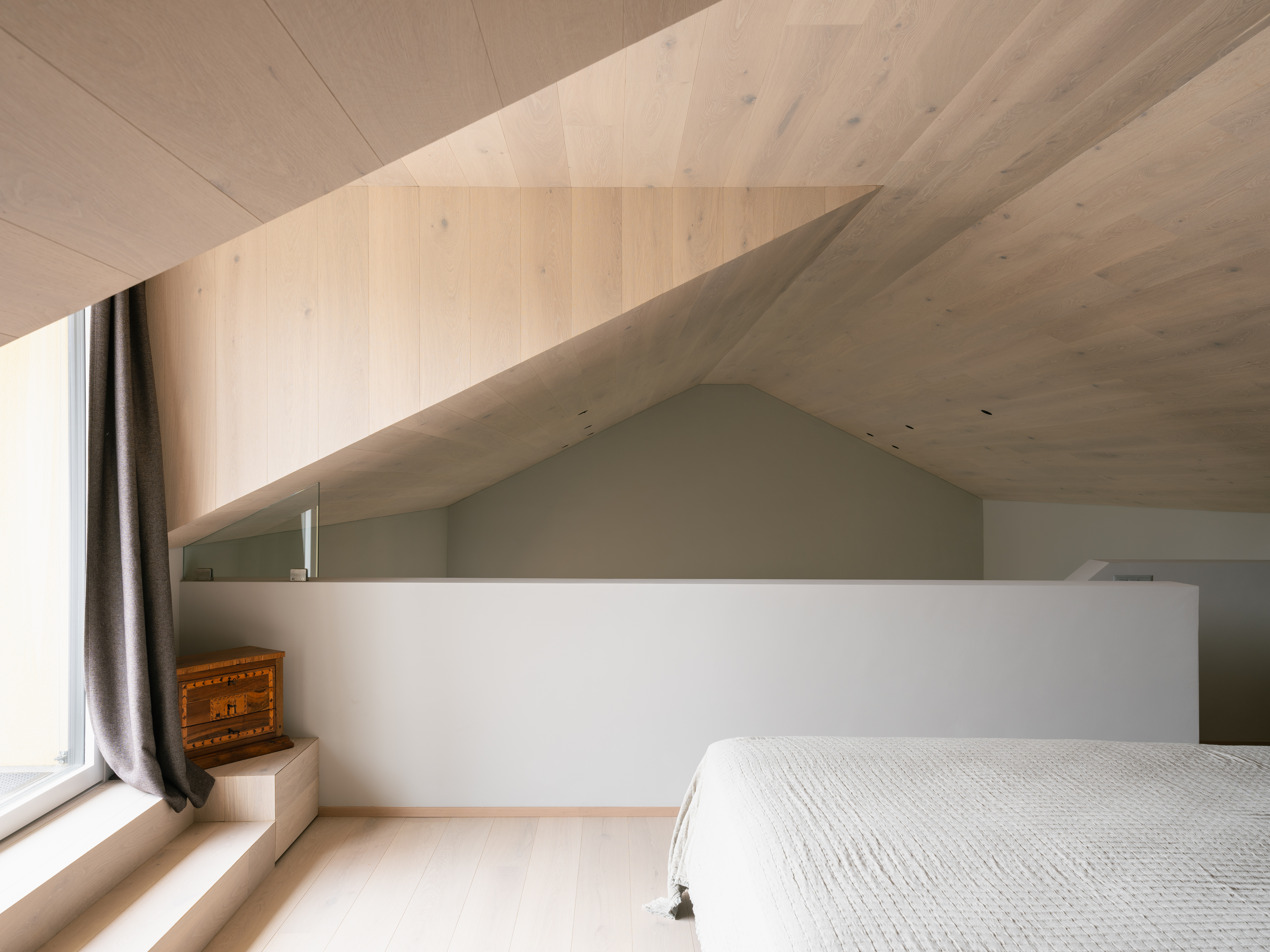 Minimalist bedroom with light wood surfaces, a sloped ceiling, and built-in custom carpentry integrated into the interior.