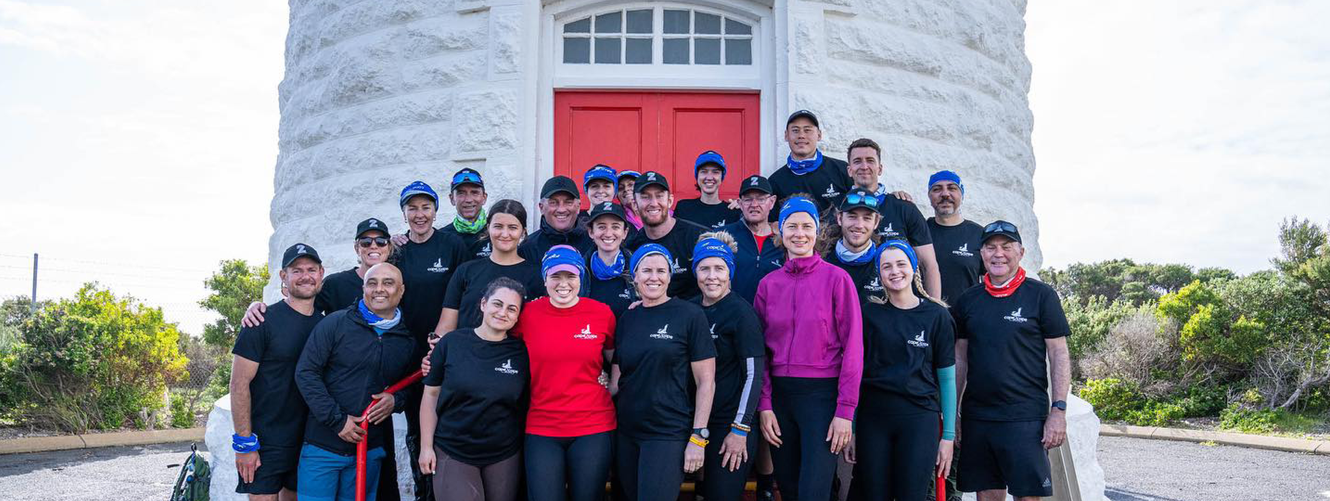 "Group photo of team members gathered outside a white lighthouse with a red door, representing Scott Bader's community initiatives." [G]